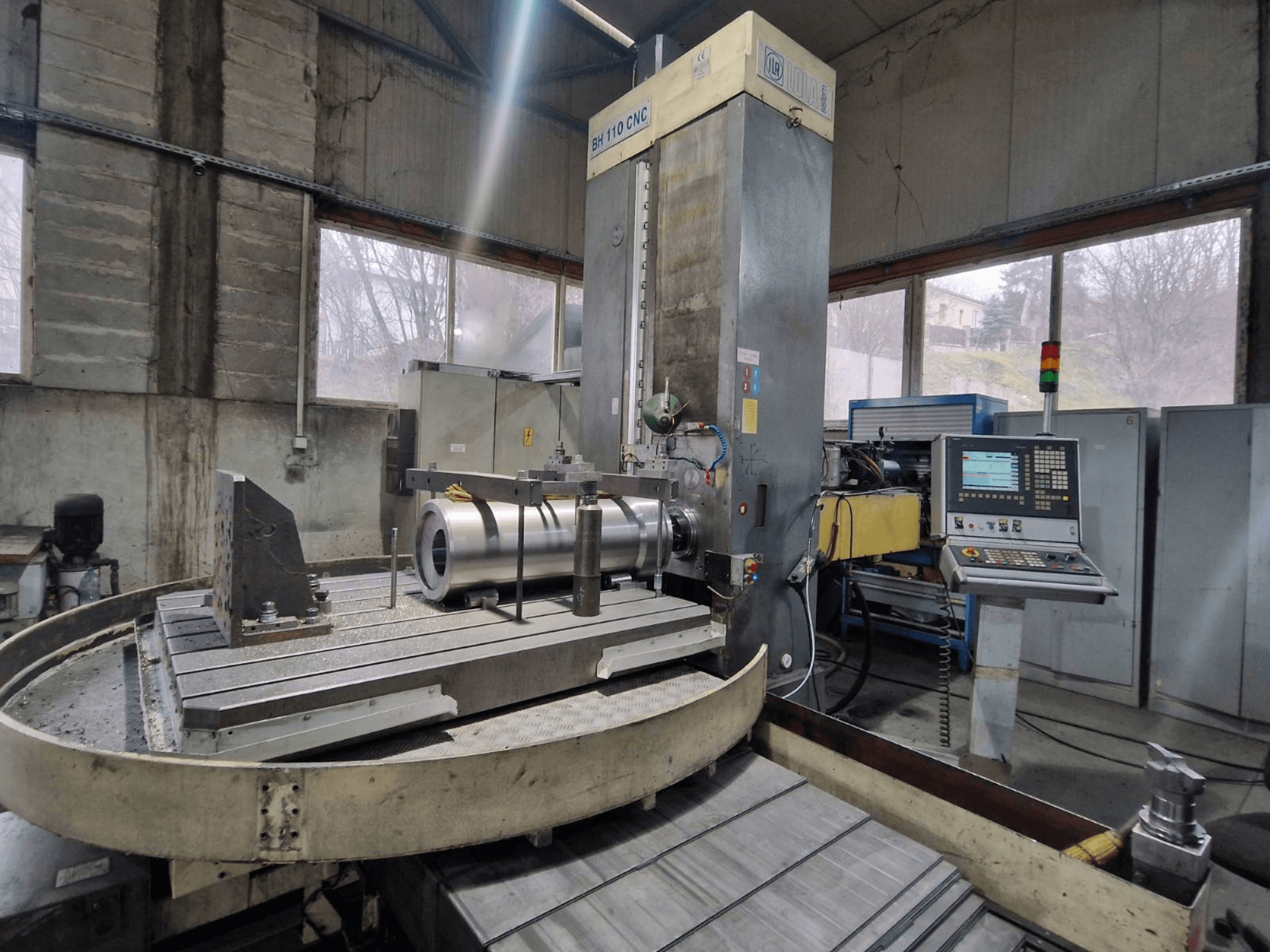 Розточувальний верстат з ЧПК LOLA BH 110 в майстерні, вид спереду, з металевою заготовкою та панеллю керування.