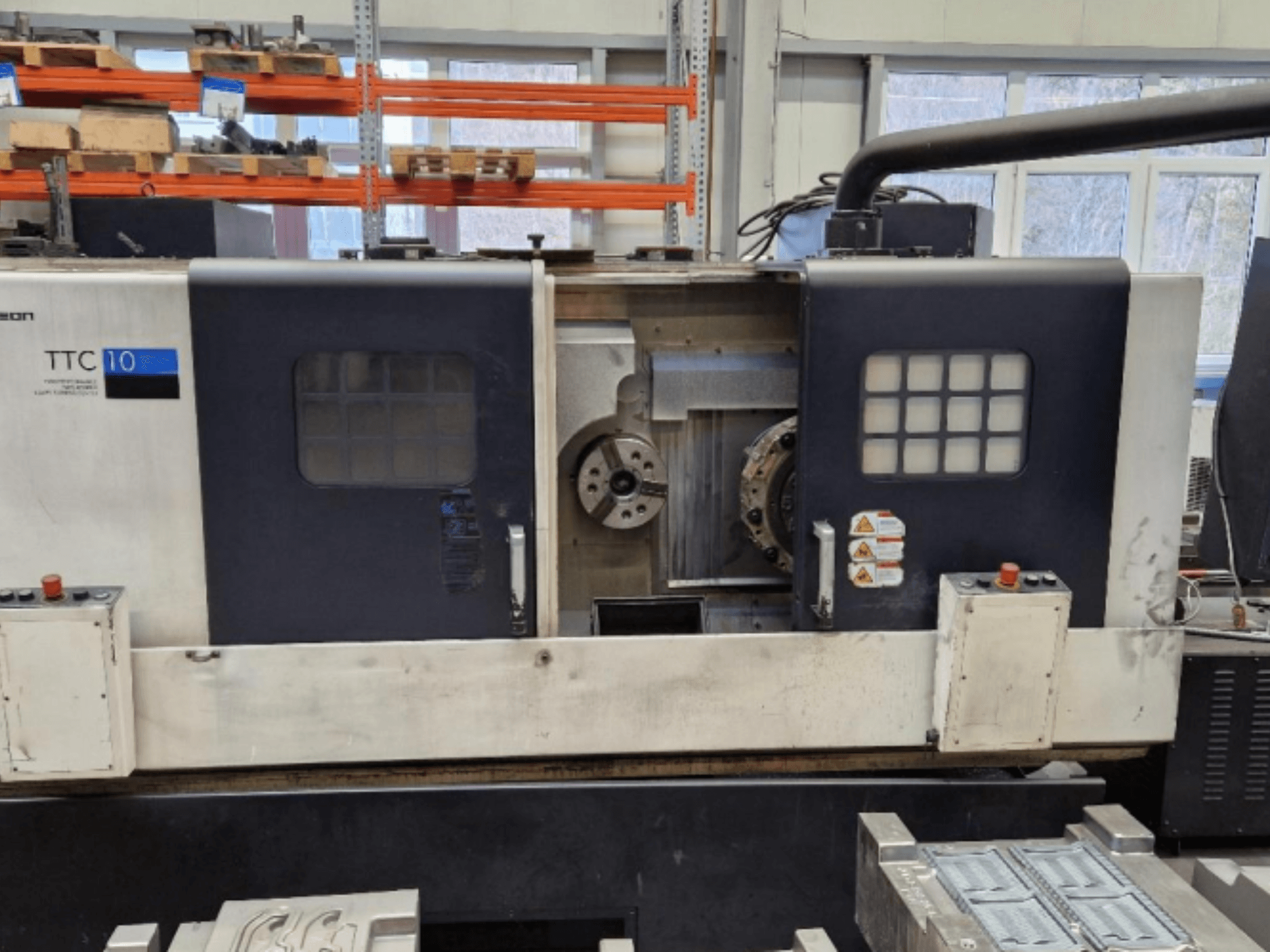 Токарний верстат TTC 10 спереду, з панеллю керування, видимими патронами та робочим простором з металевими деталями.
