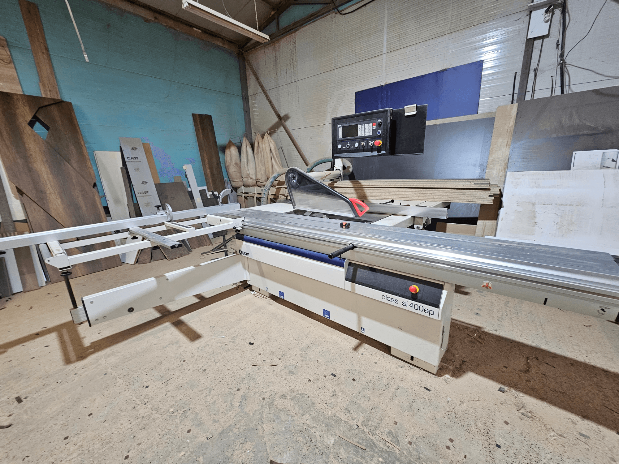 Панельна пила класу SI400EP, вид спереду, з регульованою огорожею, встановлена на піщаній підлозі майстерні, оточена дерев'яними панелями.