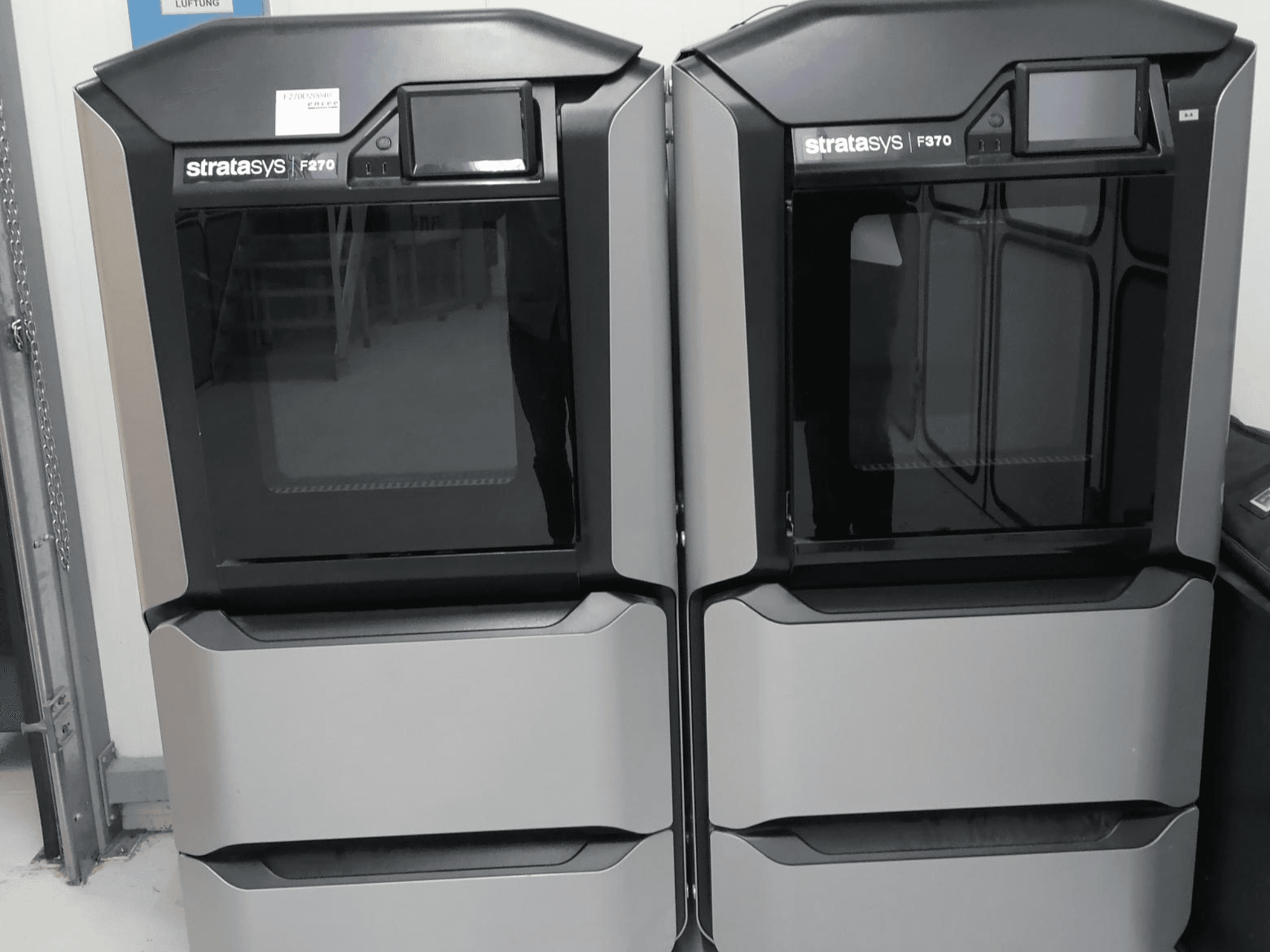 Здвоєні пластикові 3D-принтери Stratasys F370, показані спереду, вирізняються елегантним чорно-сріблястим дизайном і екранами керування.