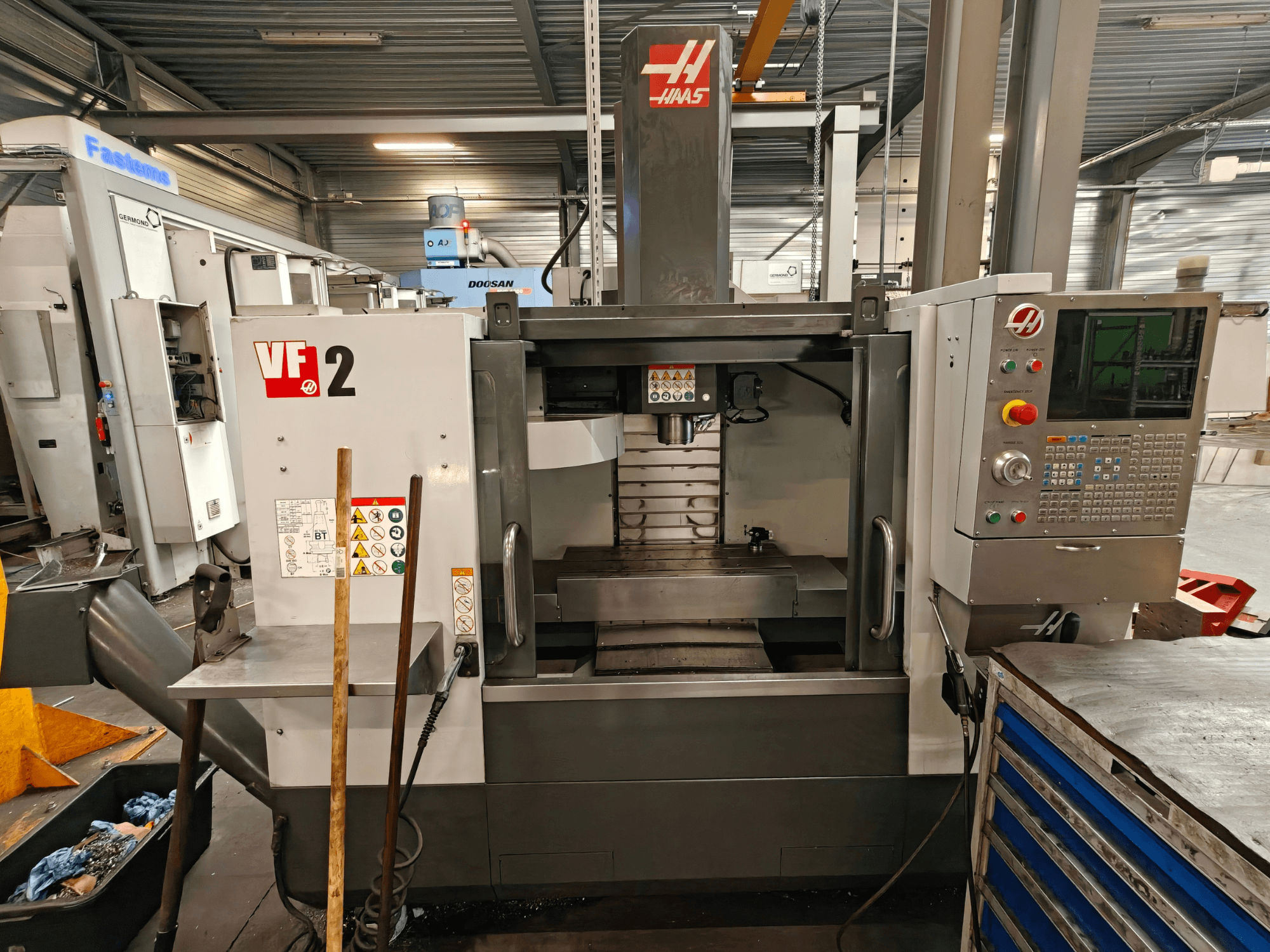 Вертикальний обробний центр HAAS VF-2, вид спереду, на якому показані елементи управління, шпиндель та робочий стіл у цехових умовах.