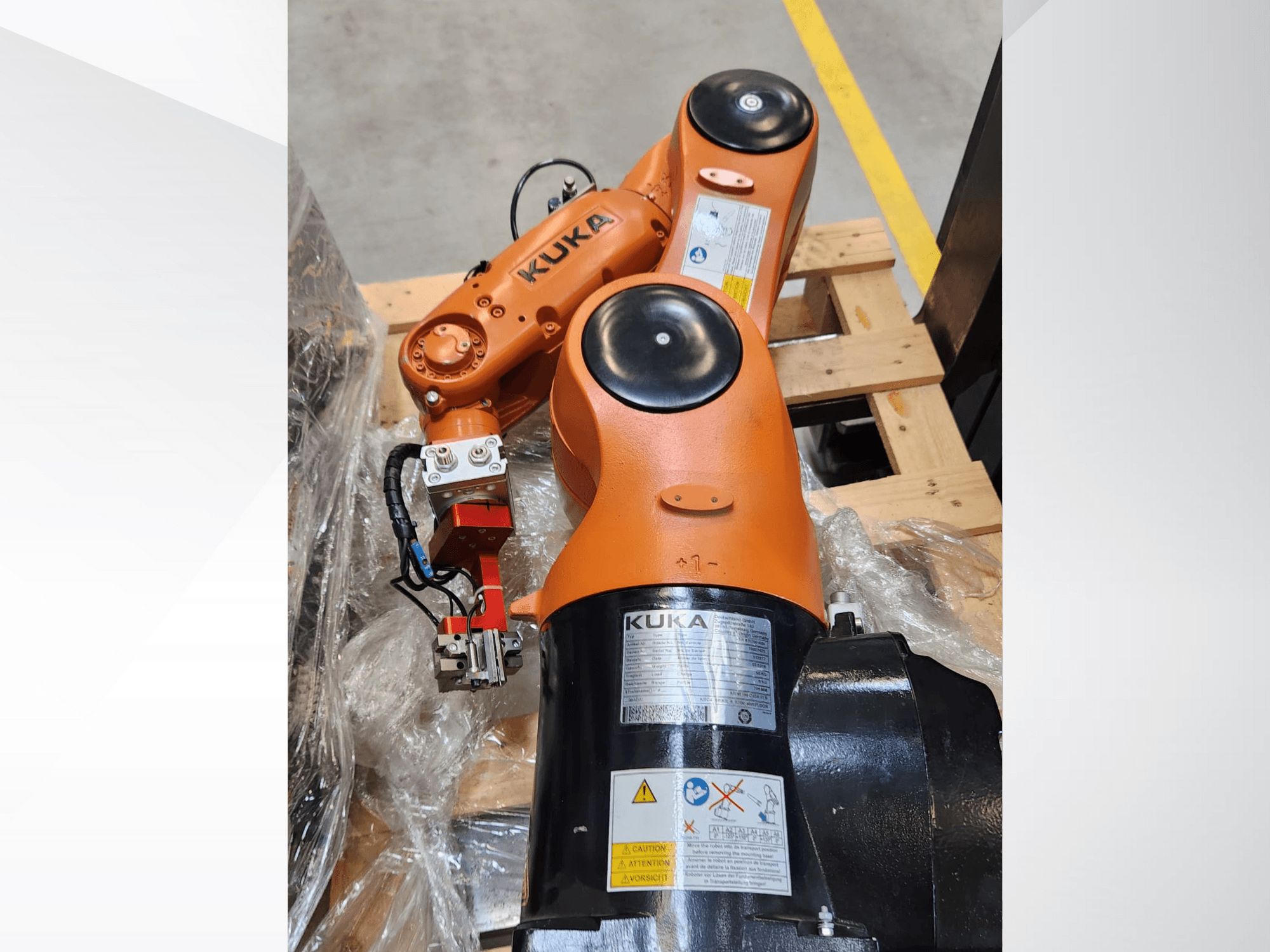 Роботизований маніпулятор KUKA з помаранчевим покриттям, вид збоку, із захватом і проводкою управління на дерев'яному піддоні.