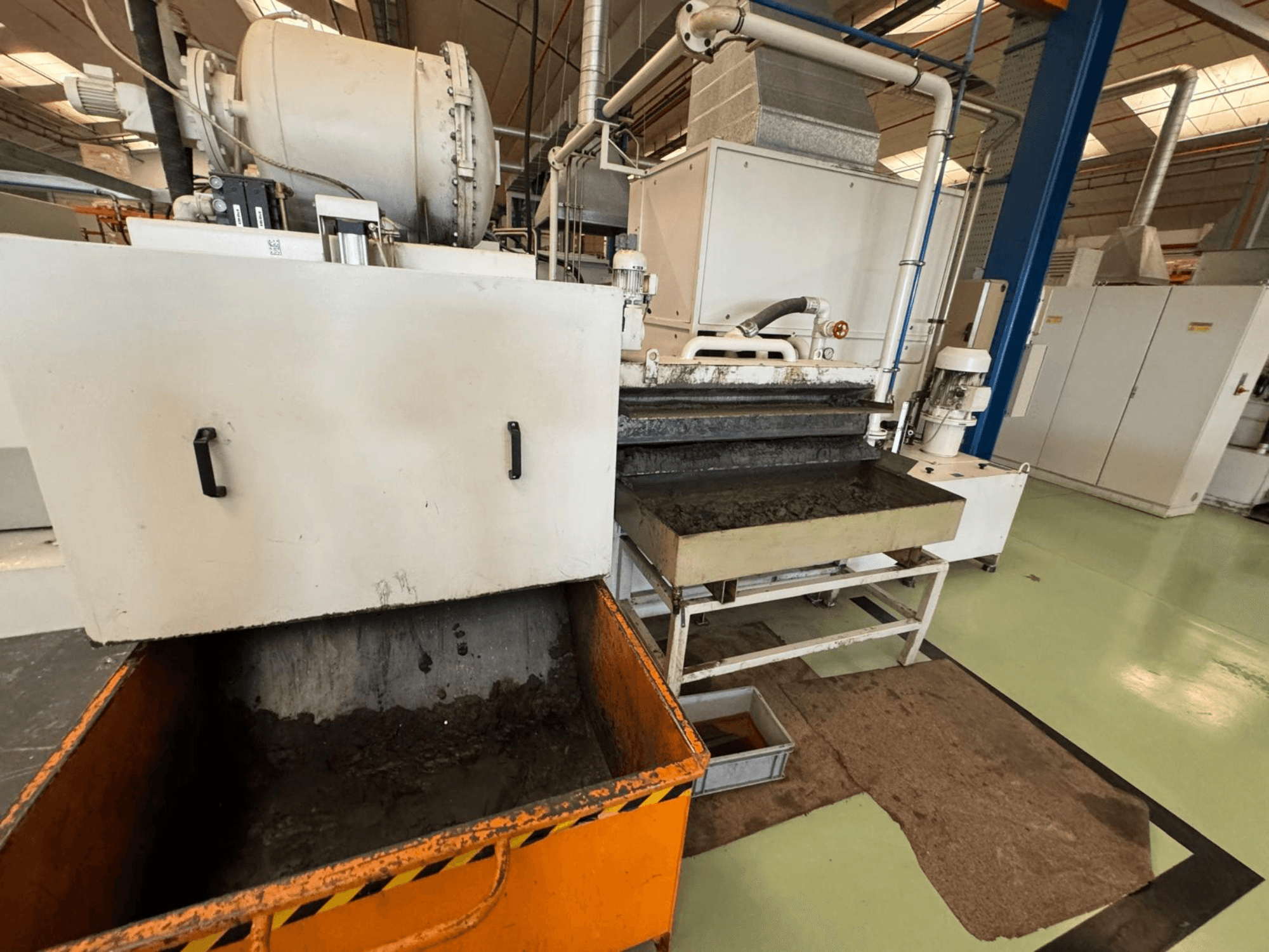 Промислове переробне обладнання з помаранчевим контейнером для відходів, вид спереду; містить двигун, конвеєри та зону технічного обслуговування.