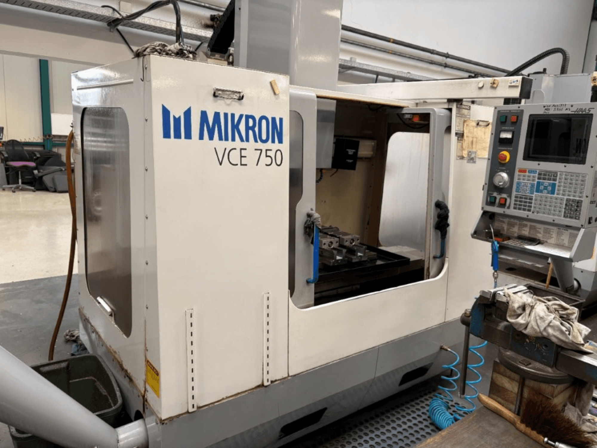 Фрезерний верстат з ЧПК Mikron VCE 750 вид спереду, з обробленим робочим столом і панеллю керування з різними кнопками та екранами.