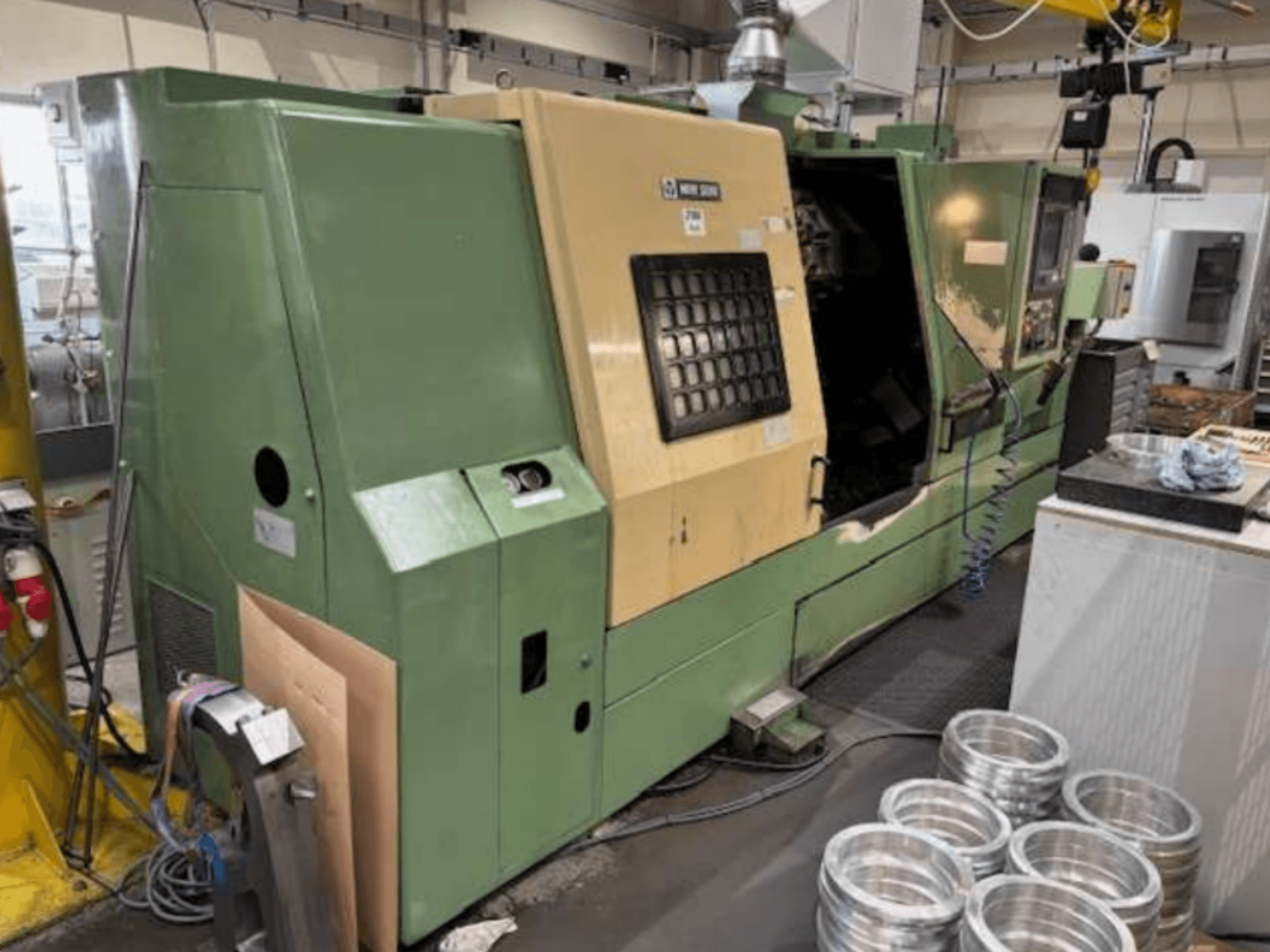 Зелений токарний верстат з ЧПУ від Mazak, вид спереду, демонструє панель управління та оброблені алюмінієві деталі на робочому столі.