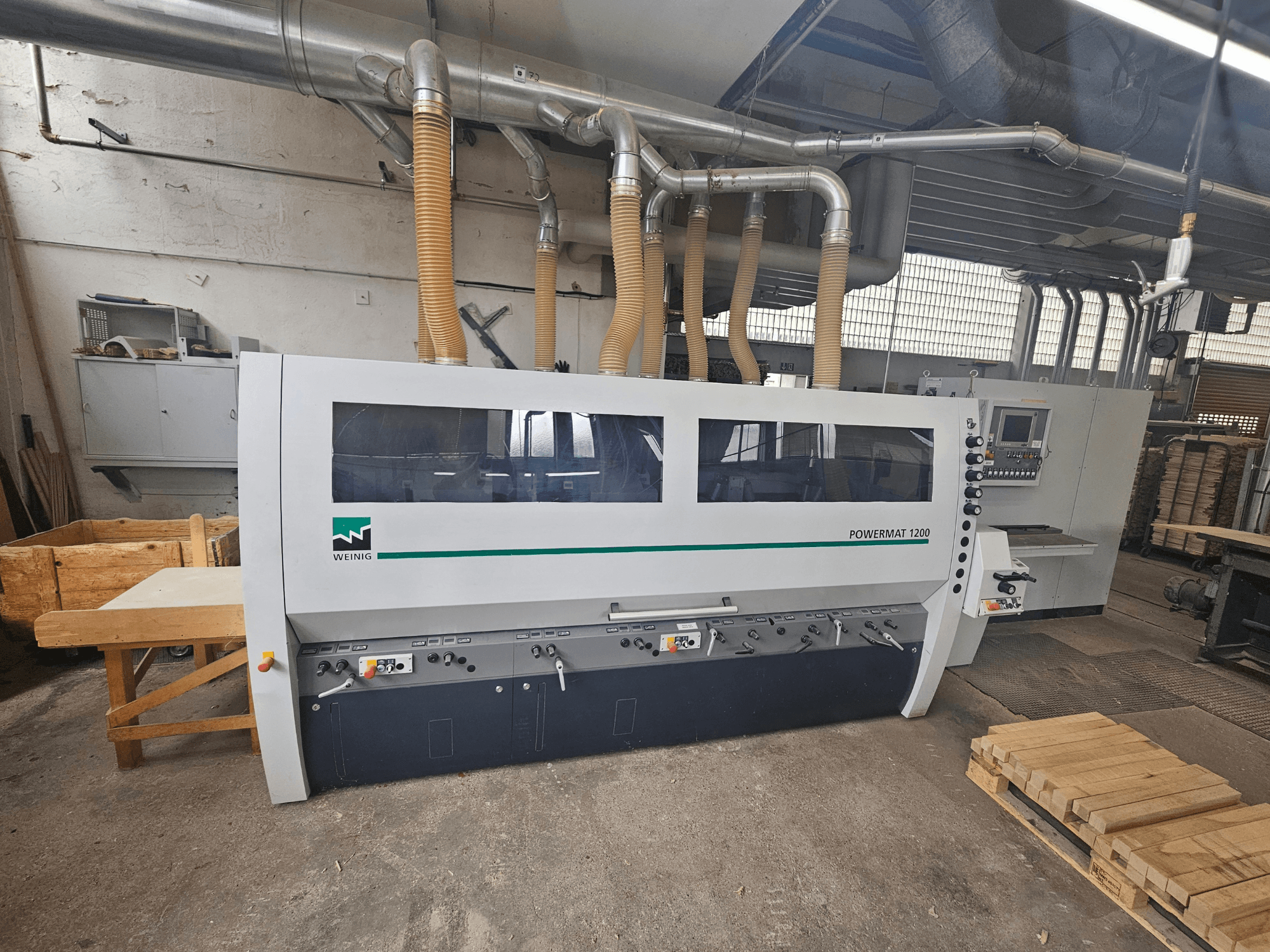 Деревообробний верстат Weinig Powermat 1200, вид спереду, з панеллю керування та штабелями деревини в умовах майстерні.