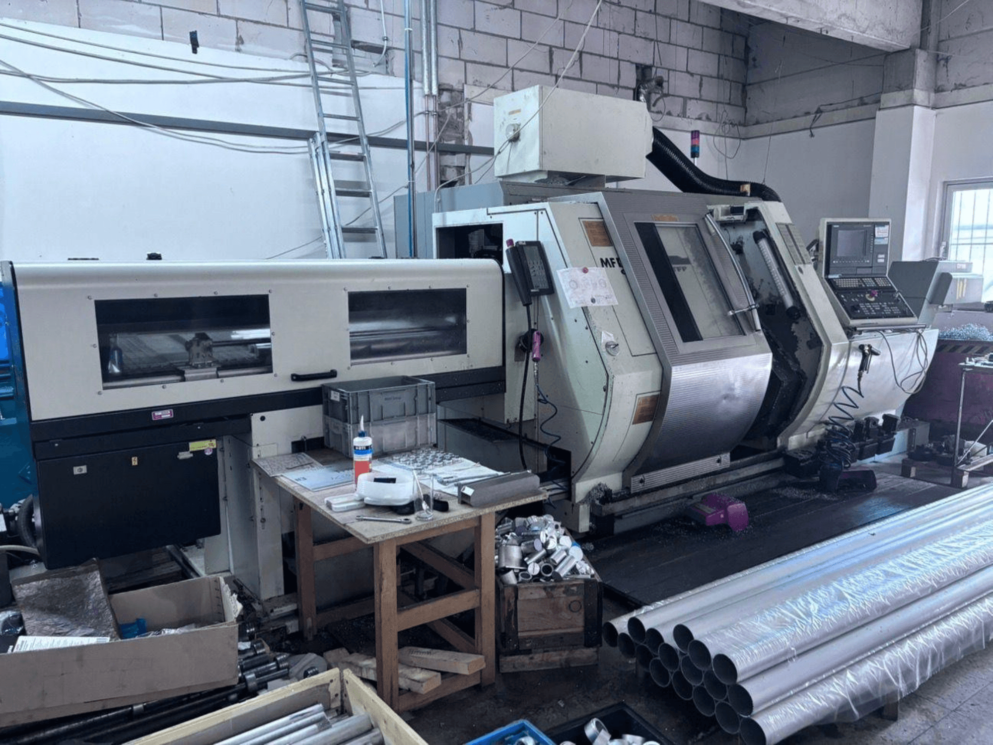 Токарно-фрезерний центр Gildemeister MF Twin 65, вид збоку, на якому видно панель управління, зону обробки та алюмінієві труби.