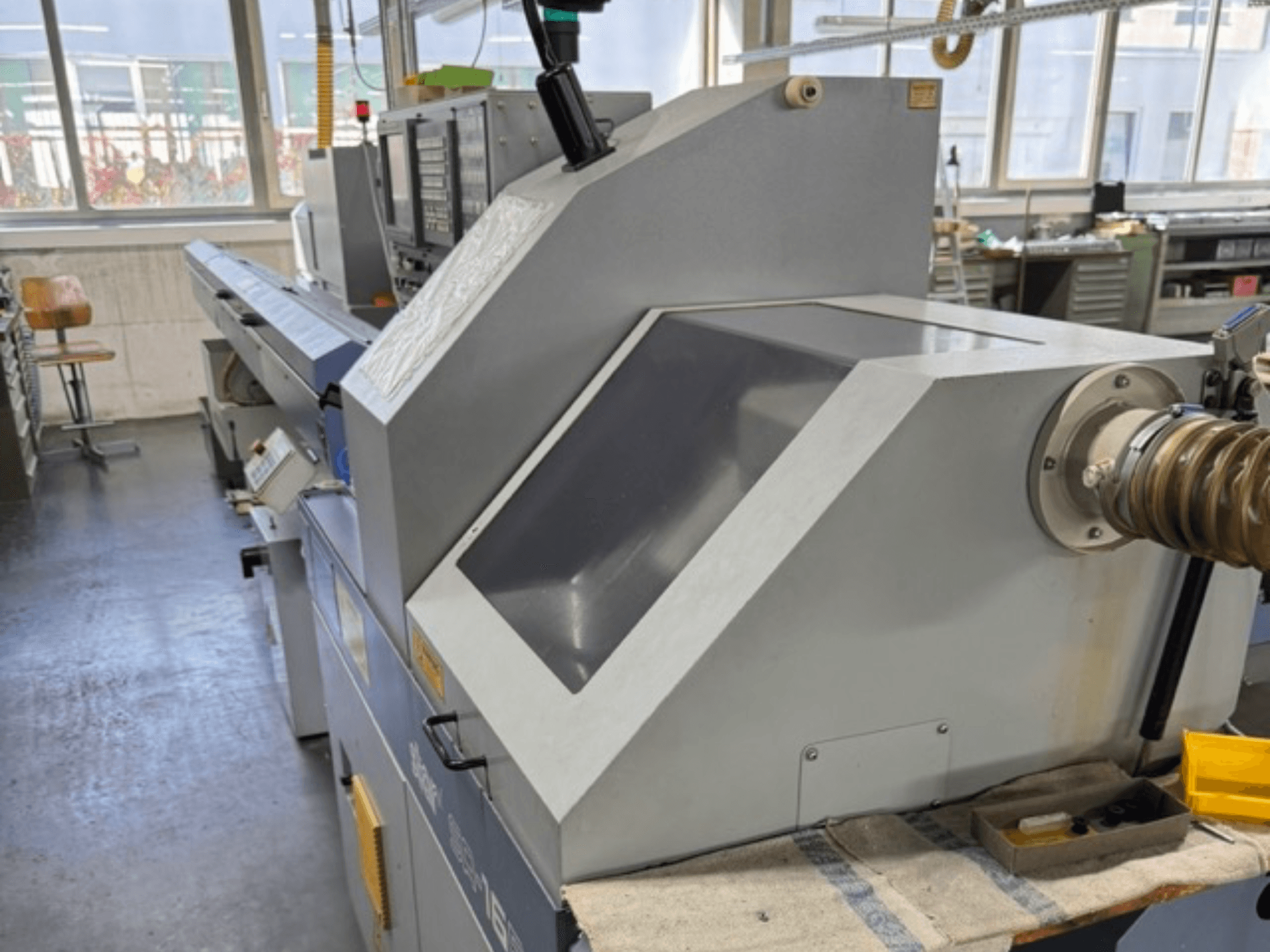 Сіра промислова машина, вигляд збоку, має велику кутову панель, кнопки керування та кріплення для шланга.