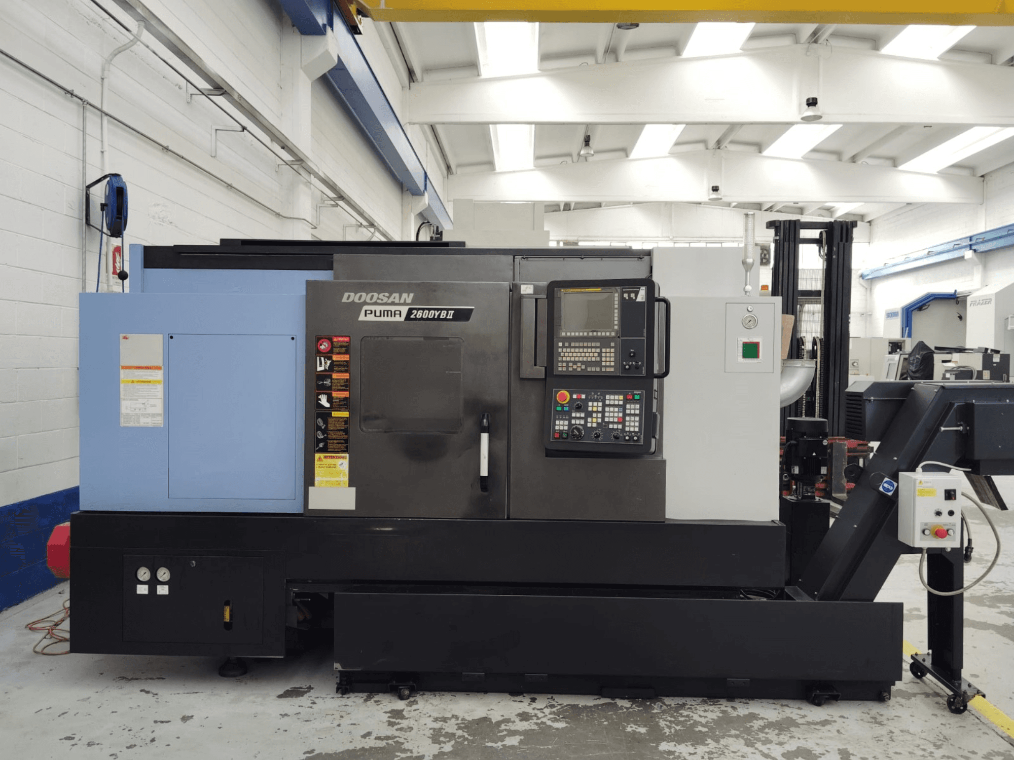 Вид спереду горизонтального токарного верстата DOOSAN Puma 2600YB II з панеллю керування та знаками безпеки.