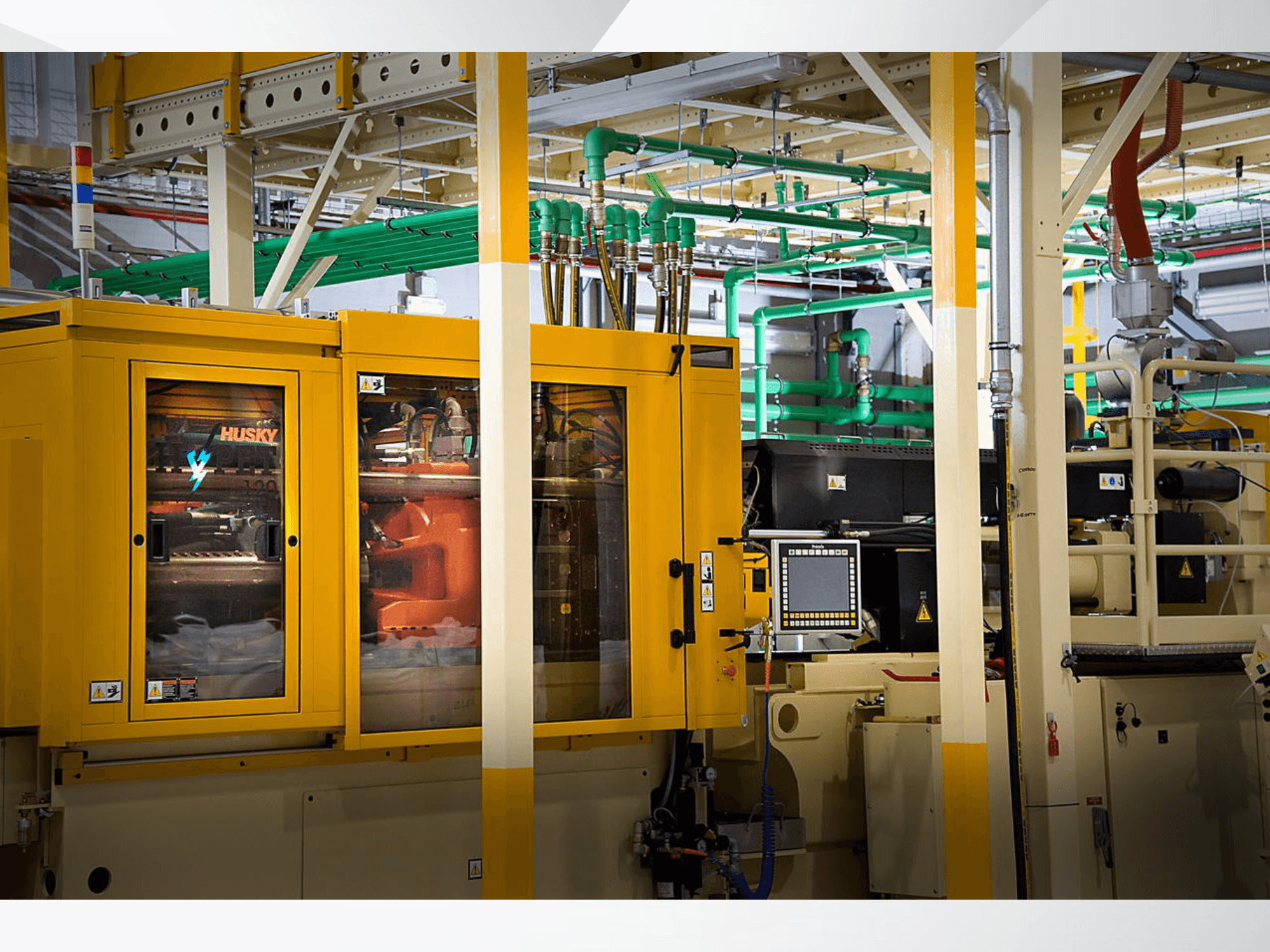 Промислова машина Husky жовтого кольору, вид спереду, що демонструє панель управління та внутрішні механізми на тлі заводу.