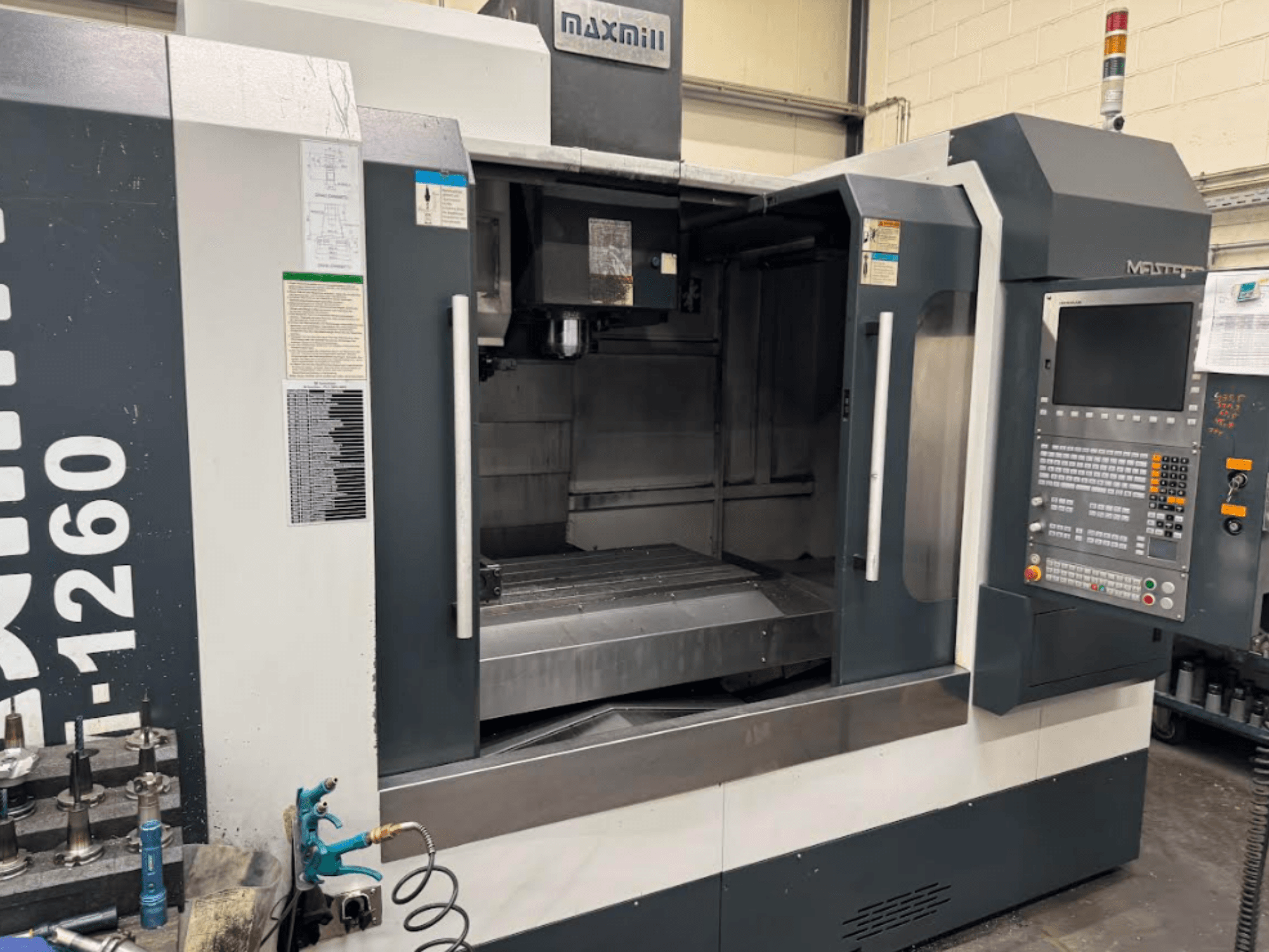 Фрезерний верстат з ЧПК Maxmill, модель M-1260, вид спереду: порожній робочий простір з панеллю керування та інструкцією з експлуатації.