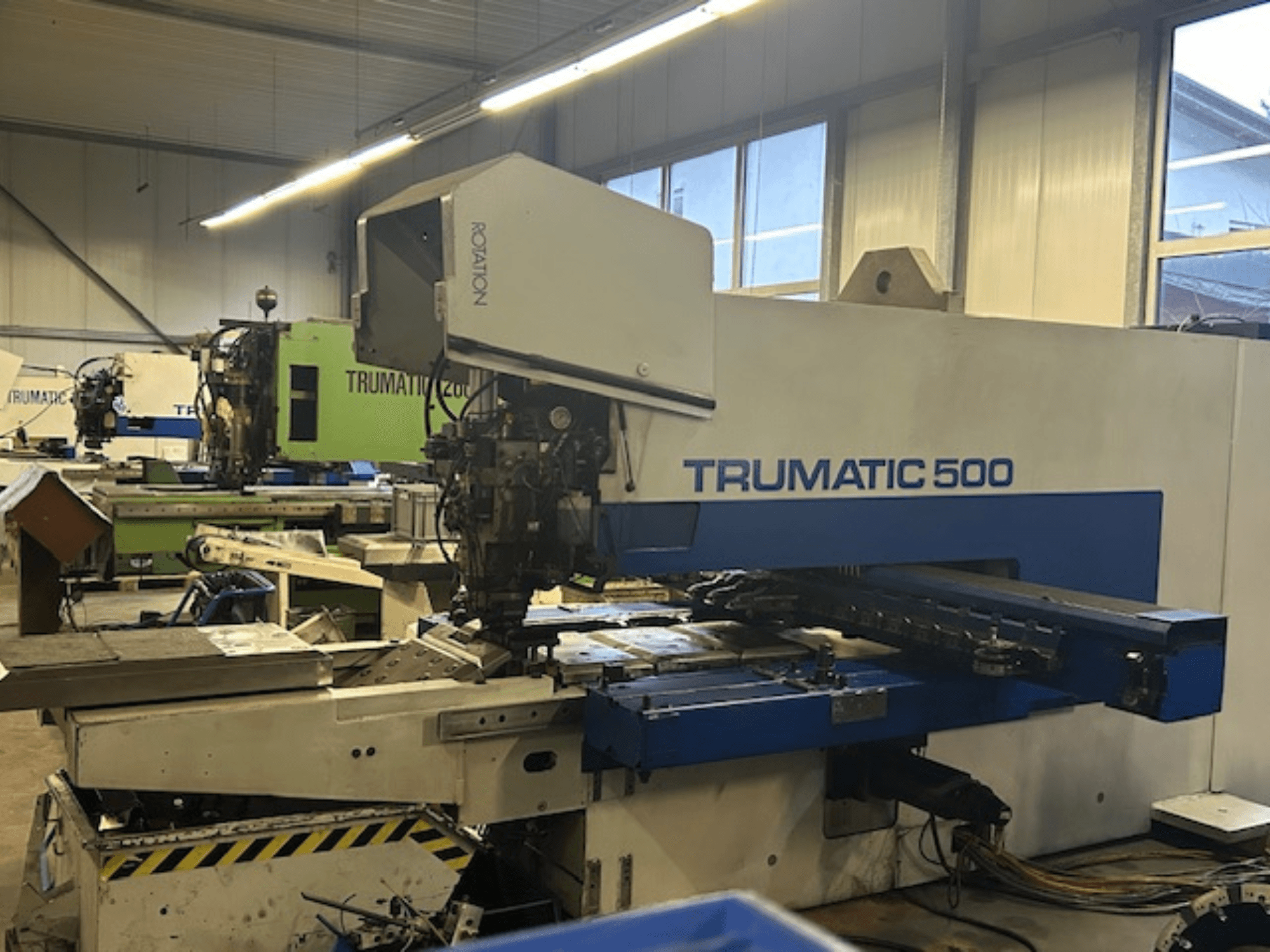 Пробивний верстат з ЧПК TRUMPF TRUMATIC 500, вид спереду, з панеллю керування та механічними частинами. Обстановка промислового цеху.