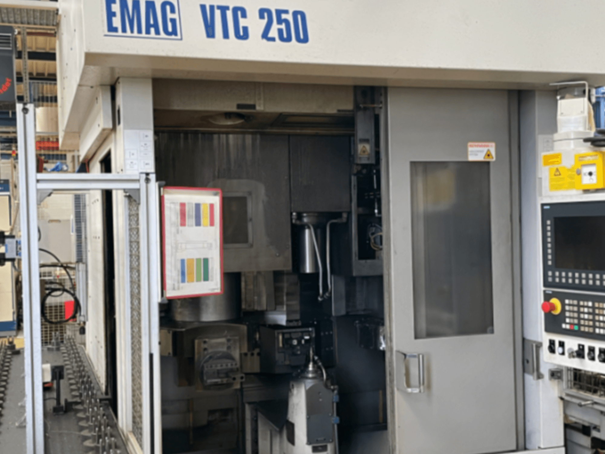 Вигляд спереду вертикального токарного верстата EMAG VTC 250, на якому видно панель управління, робочий інтерфейс та відкриті дверцята доступу.