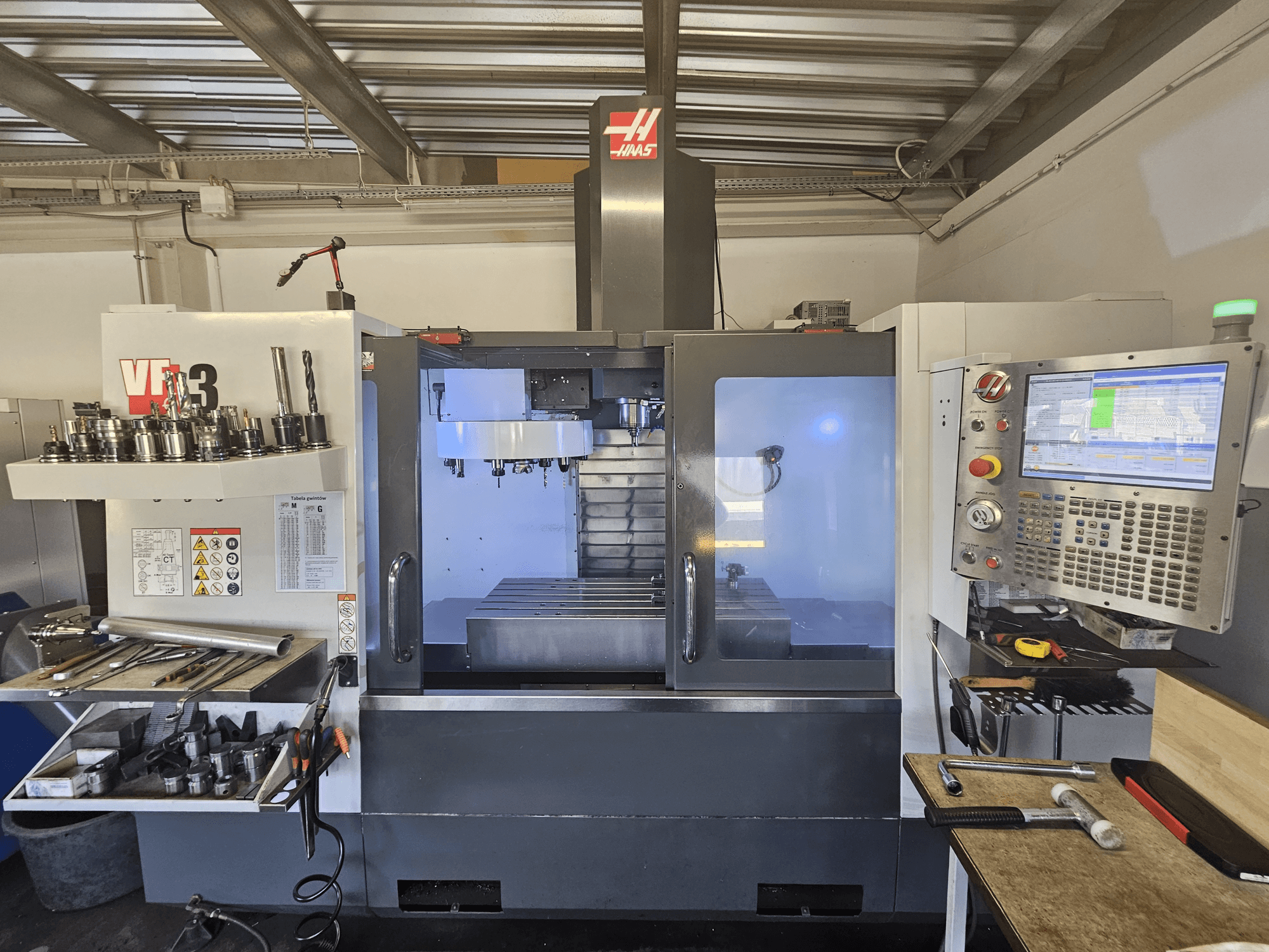 Верстат з ЧПК Haas VF-3 в майстерні, вид спереду, де показані інструменти, елементи керування та зона фрезерування з підсвічуванням.