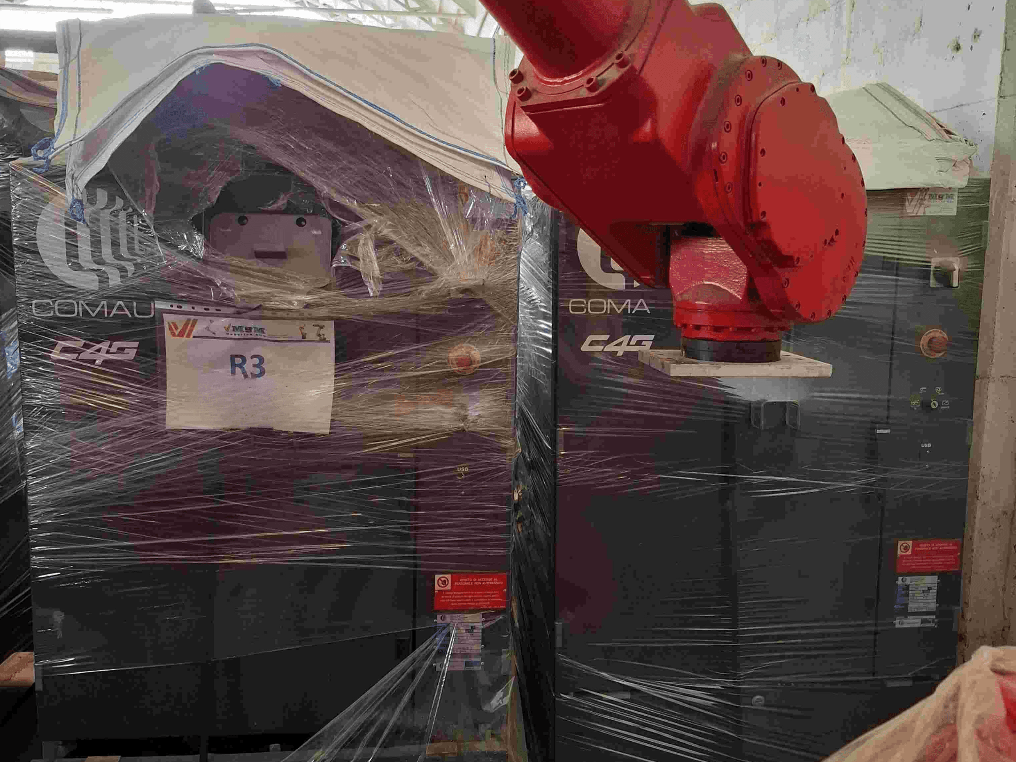 Роботизована рука Comau C4G спереду, загорнута в пластик, з маркуванням "R3", з попереджувальними наклейками на машині.