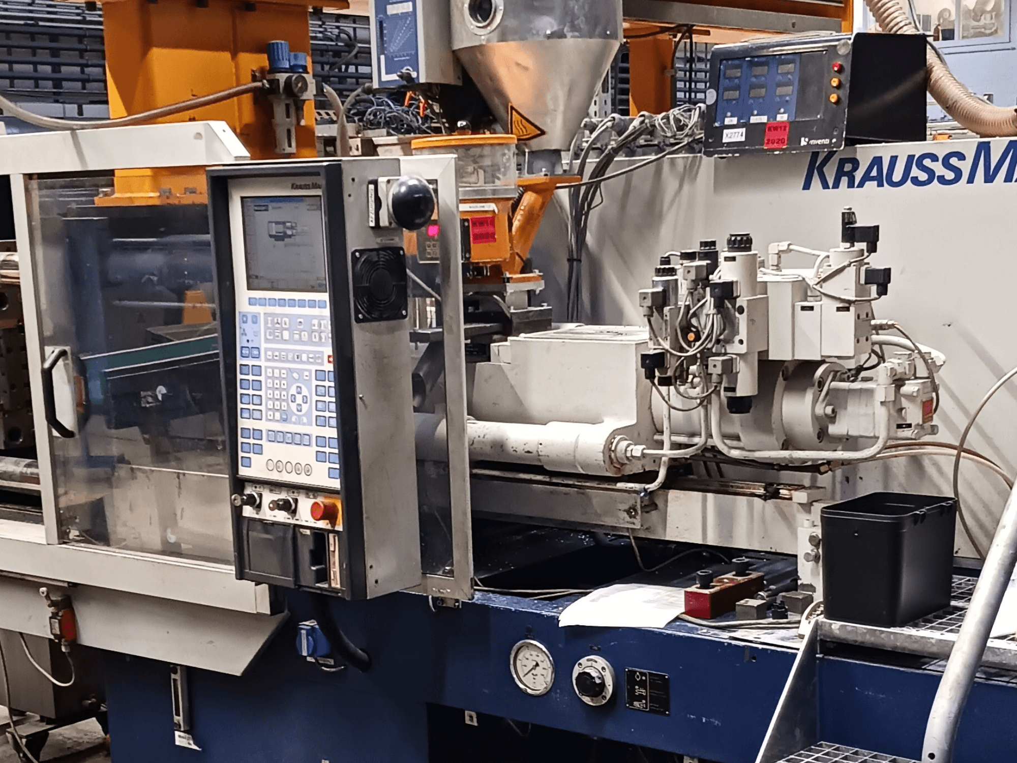 Термопластавтомат KraussMaffei з панеллю керування, гідравлічними вузлами та інструментами на передньому плані, вигляд спереду.