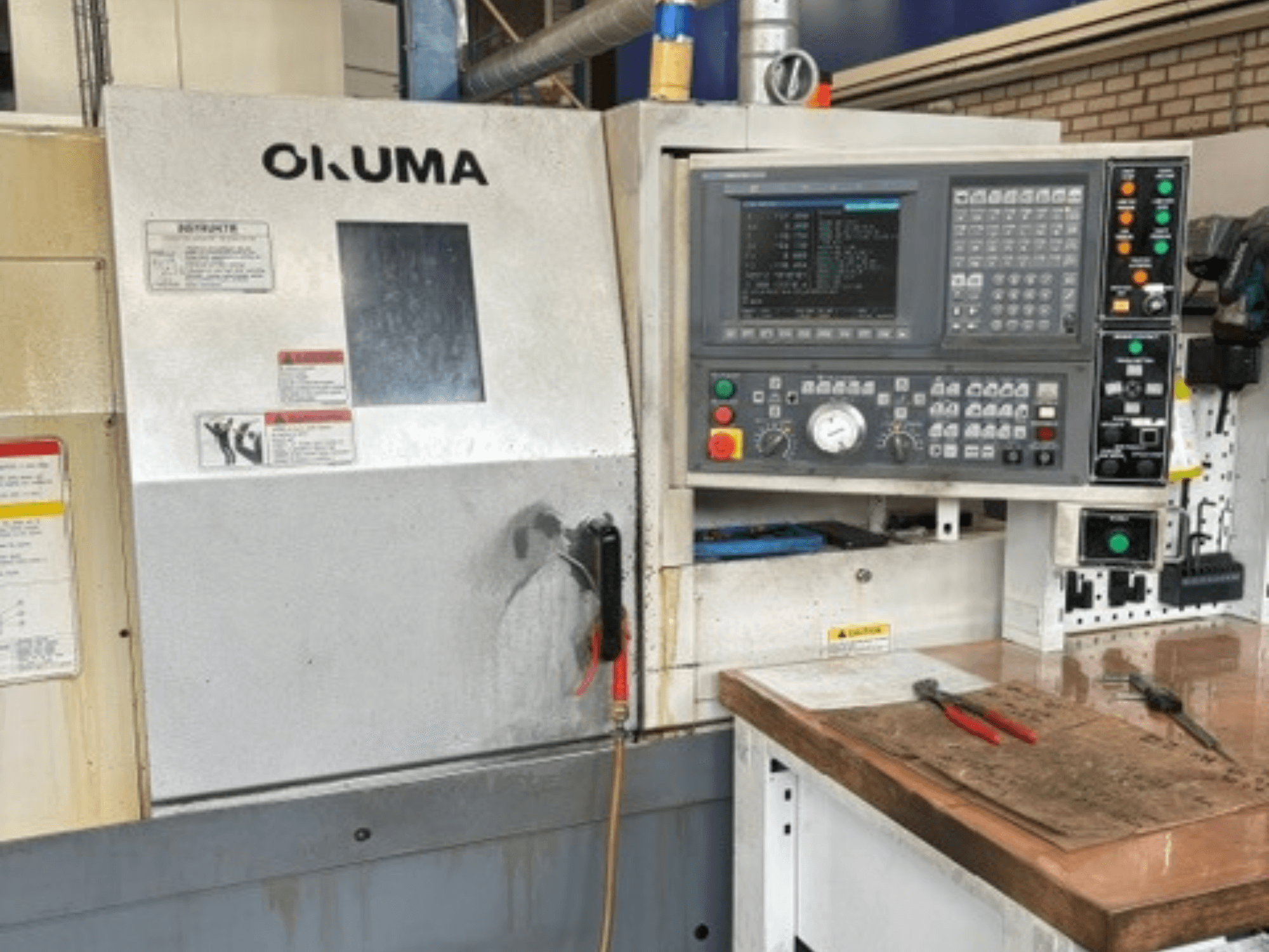 Горизонтальний токарний верстат Okuma ES-L10II у фронтальному ракурсі: на фото зображено панель керування, дисплей та робочу зону з інструментами.