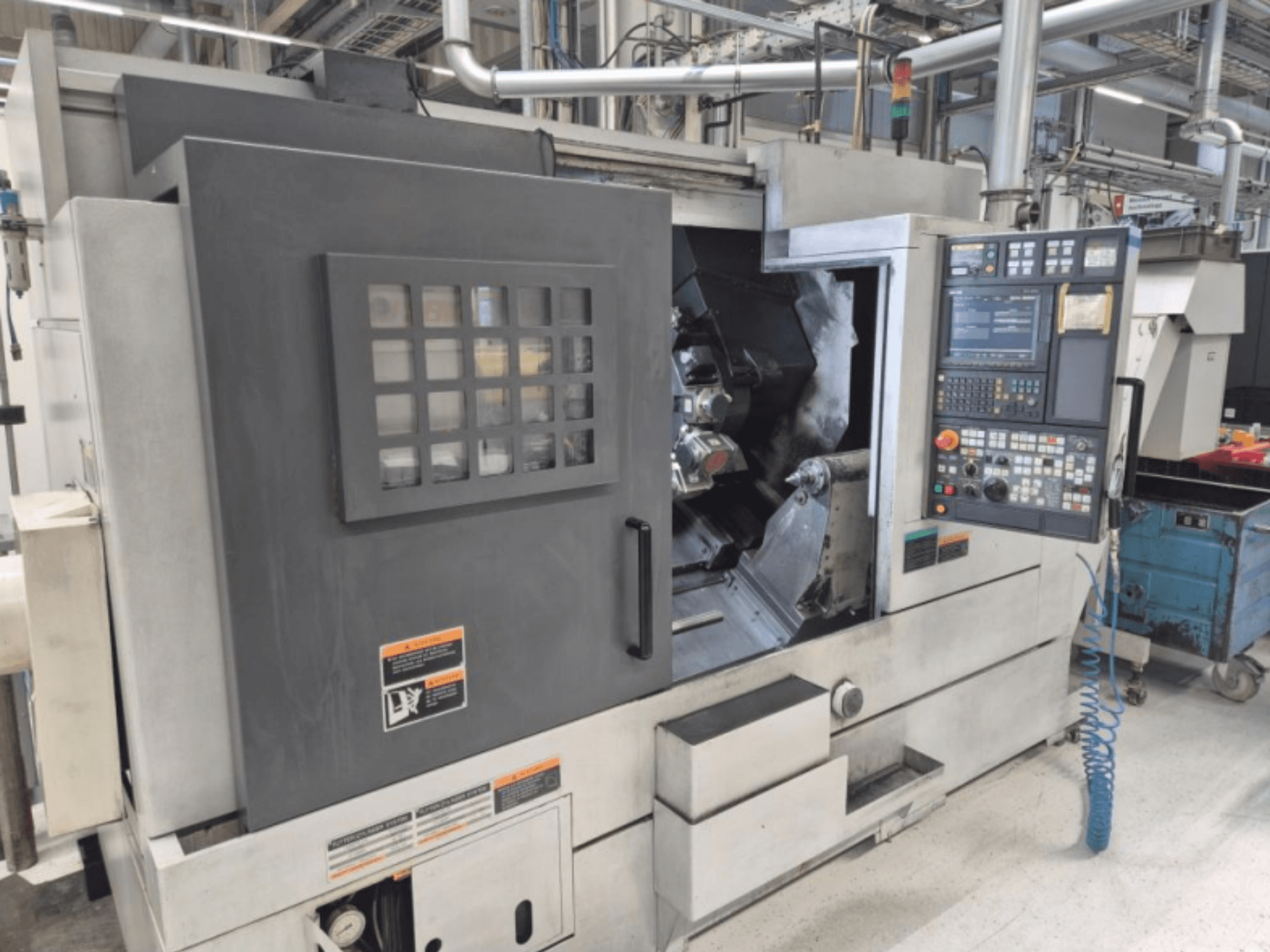 Токарний верстат з ЧПУ з панеллю керування, вигляд спереду. Має видиму робочу зону та вікно безпеки, марка невідома.