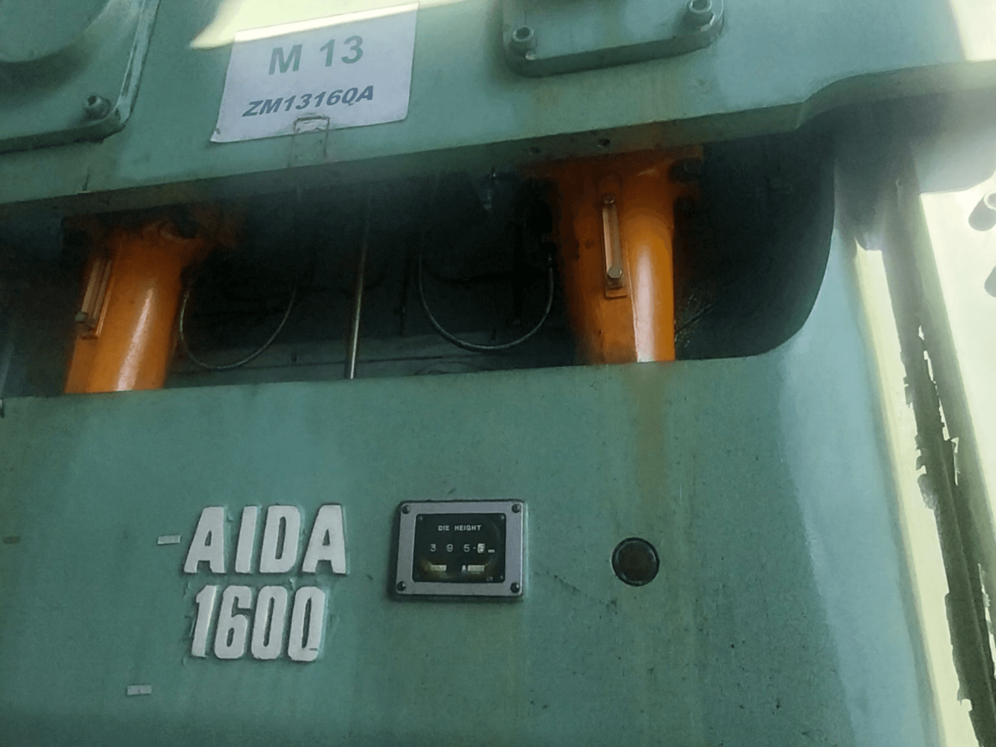 Механічний штампувальний прес AIDA NC2-1600, вид спереду; видно помаранчеві гідравлічні компоненти і датчик висоти штампа.