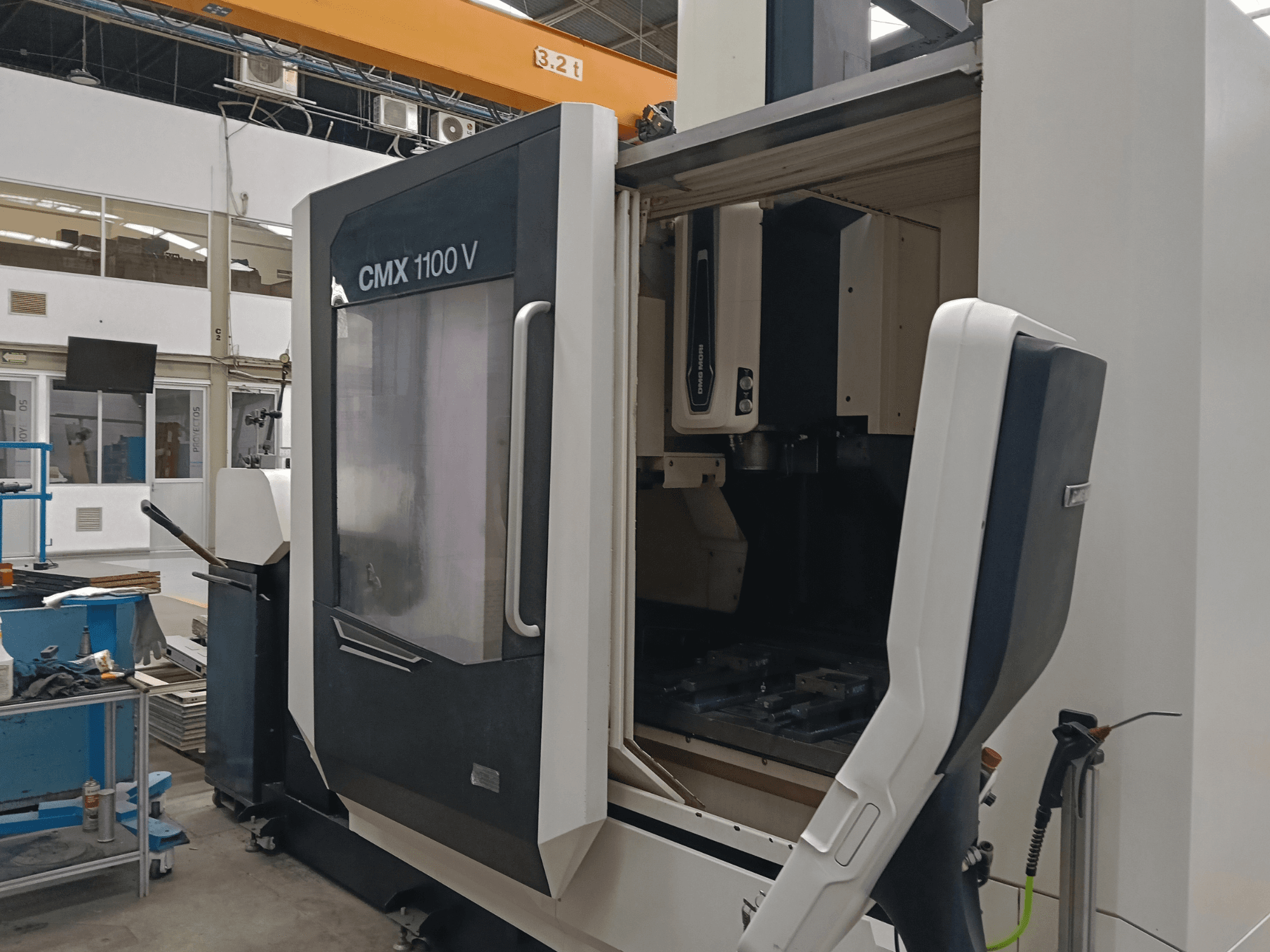 Вертикальний обробний центр DMG MORI CMX 1100 V, вид спереду з відкритими дверцятами та внутрішньою конфігурацією інструментів у промисловому приміщенні.