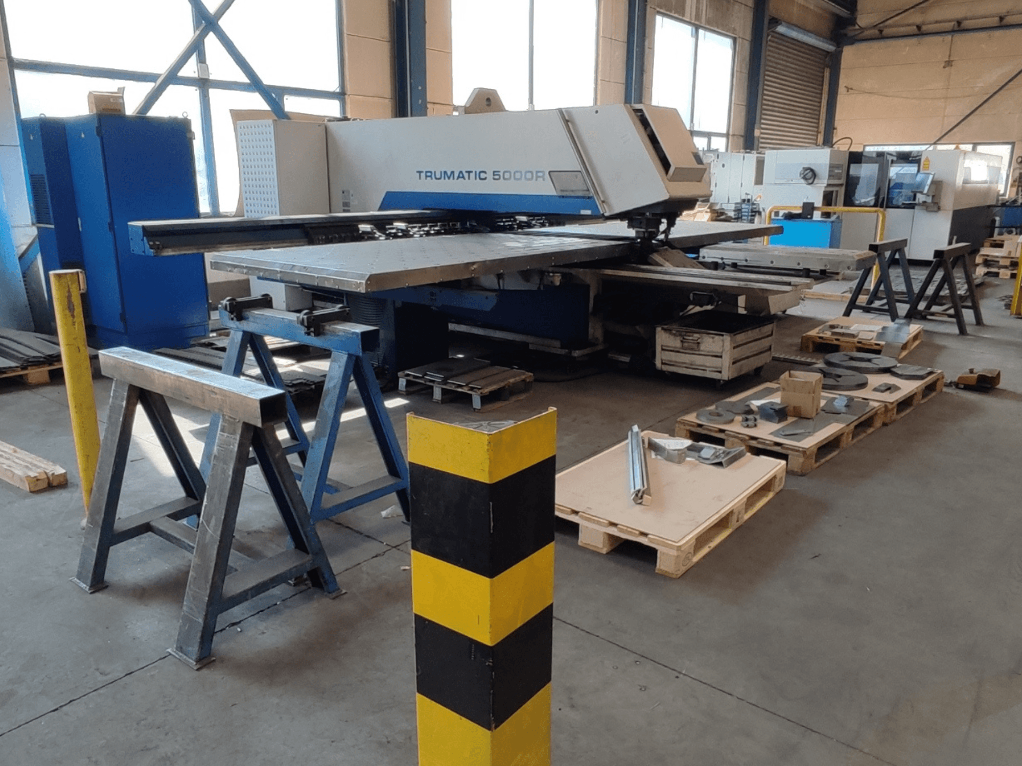 Штампувальний верстат з ЧПУ TRUMPF Trumatic 5000 R у цеху, вид збоку, поруч — інструменти та матеріали на піддонах.
