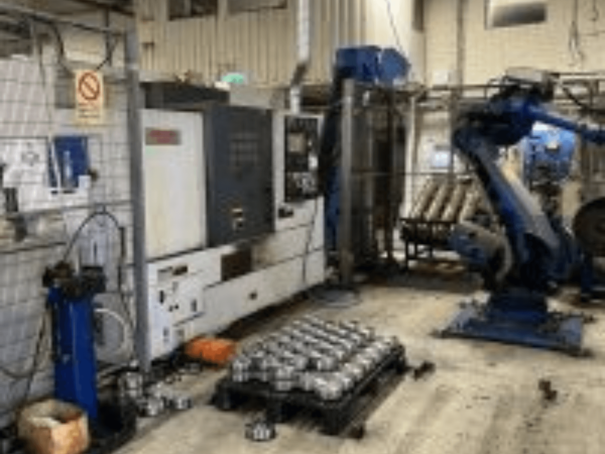 Горизонтальний вид токарного верстата MORI SEIKI NL 2500 MC/700 з роботизованою рукою та металевими деталями на підлозі.