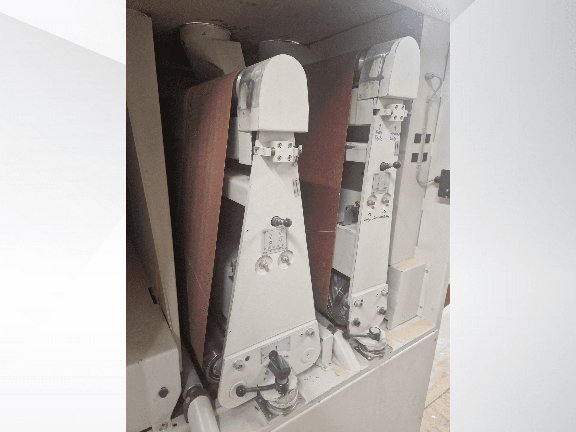 Дві промислові шліфувальні машини з червоними шліфувальними стрічками, вид спереду, демонструють елементи керування та металеві компоненти.