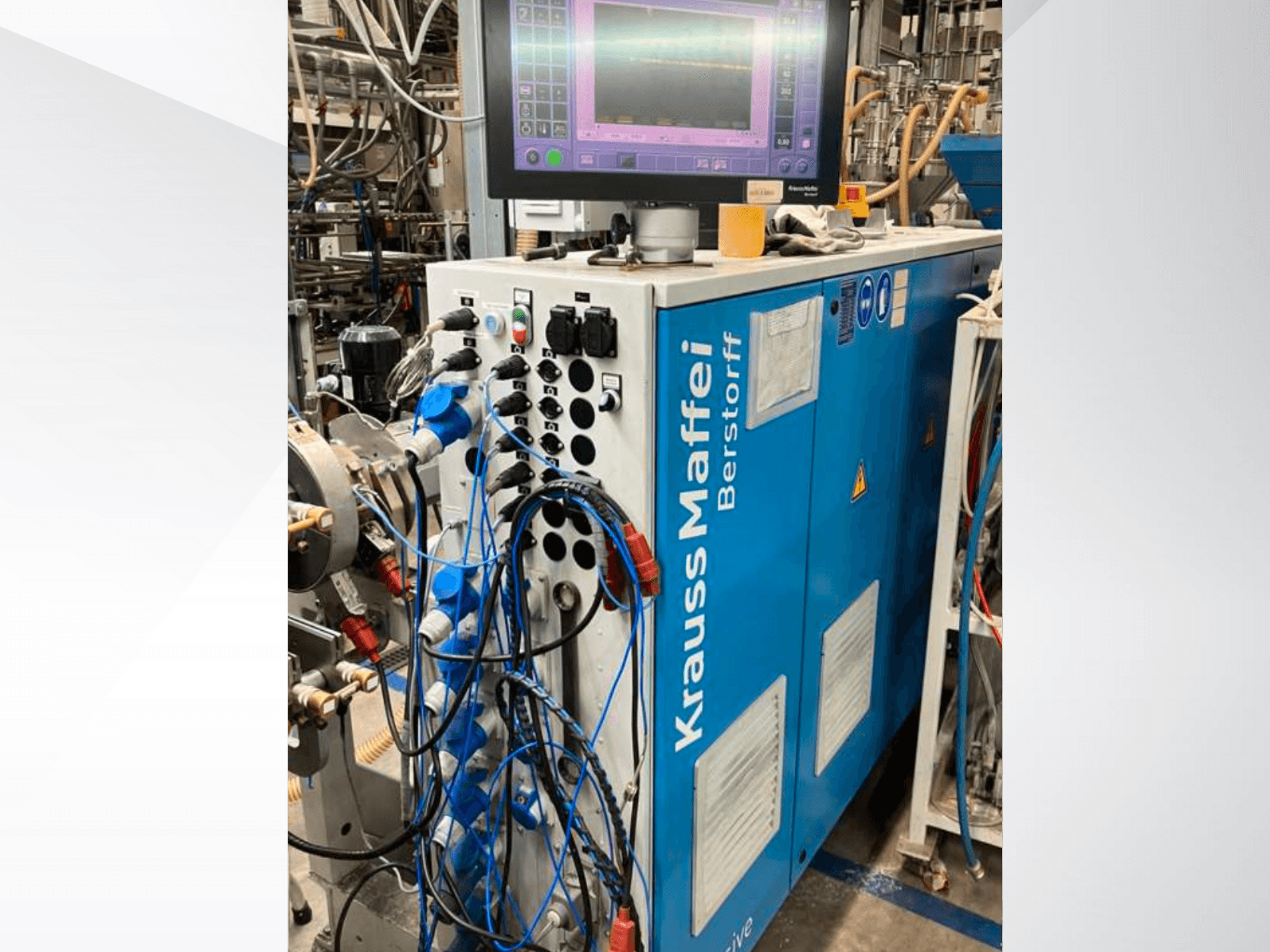 Промислова машина Krauss Maffei Berstorff з панеллю керування і монітором, з різними кнопками і підключеними шлангами, вид збоку.