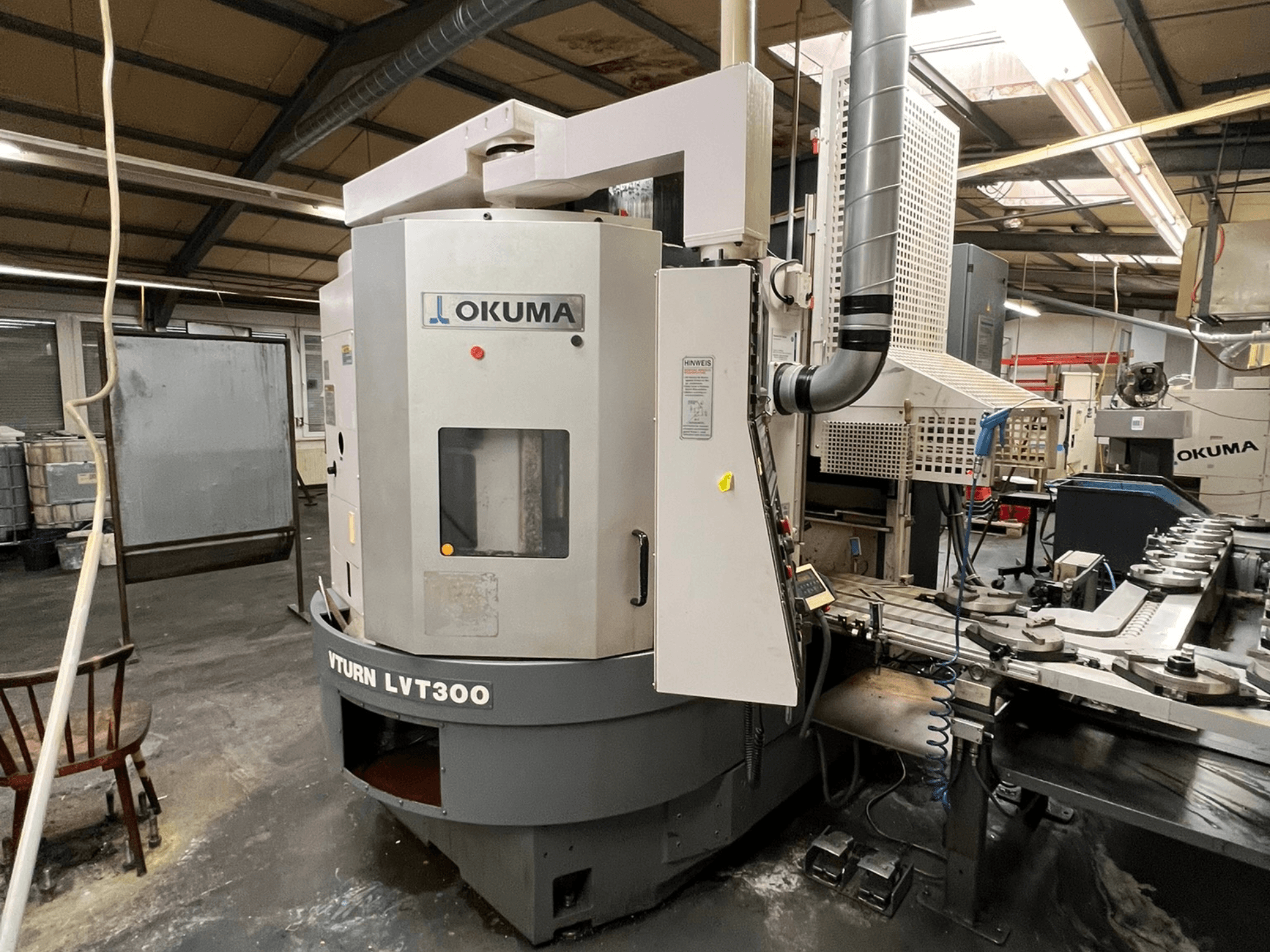 Токарний верстат з ЧПУ Okuma Vturn LVT300, вид збоку в промислових умовах, демонструє панель керування та систему охолодження.