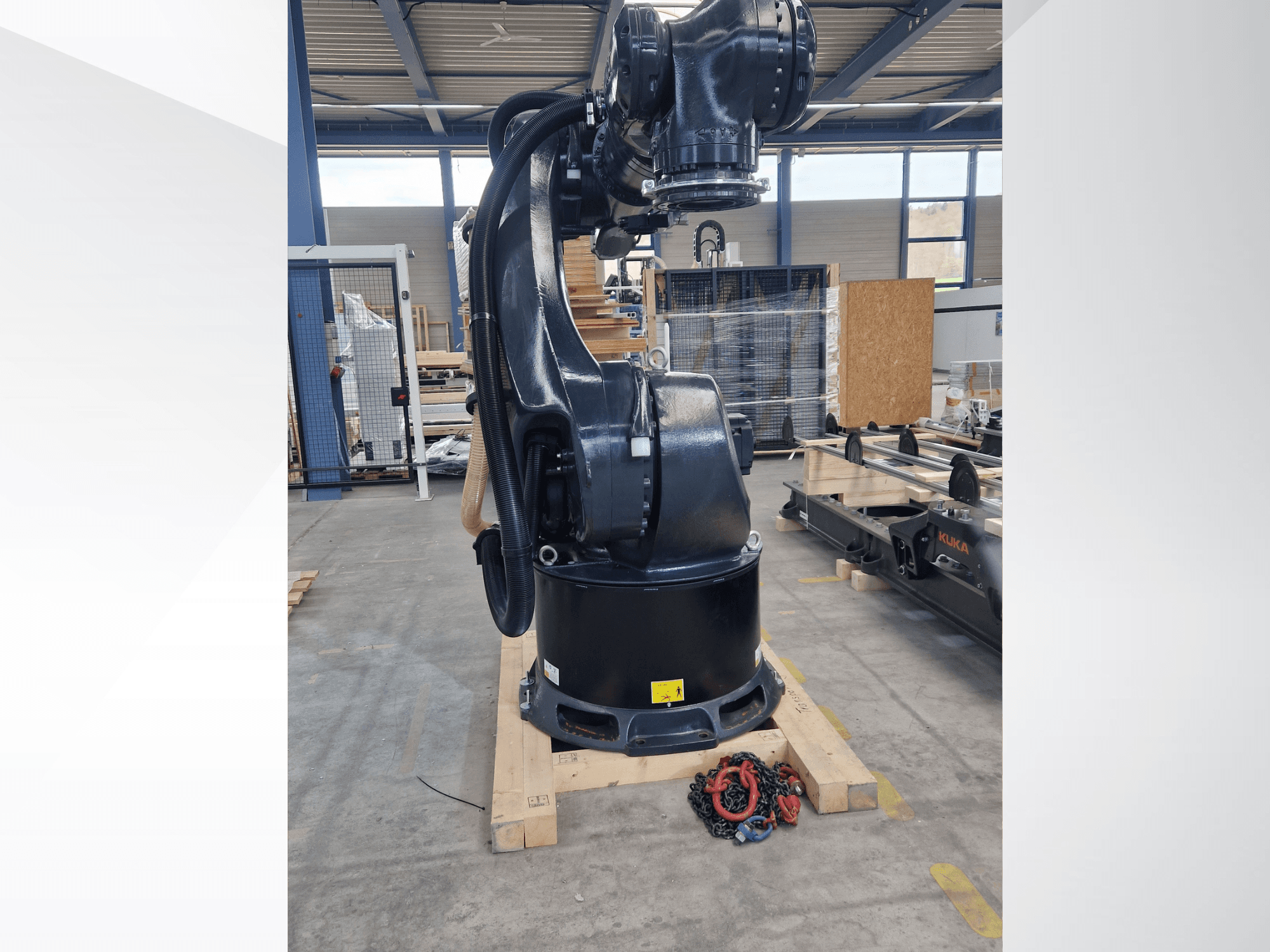 Роботизована рука KUKA KR 340 R3330 на складі; вид збоку, на якому видно її основу та кабелі, а на передньому плані — ланцюги.