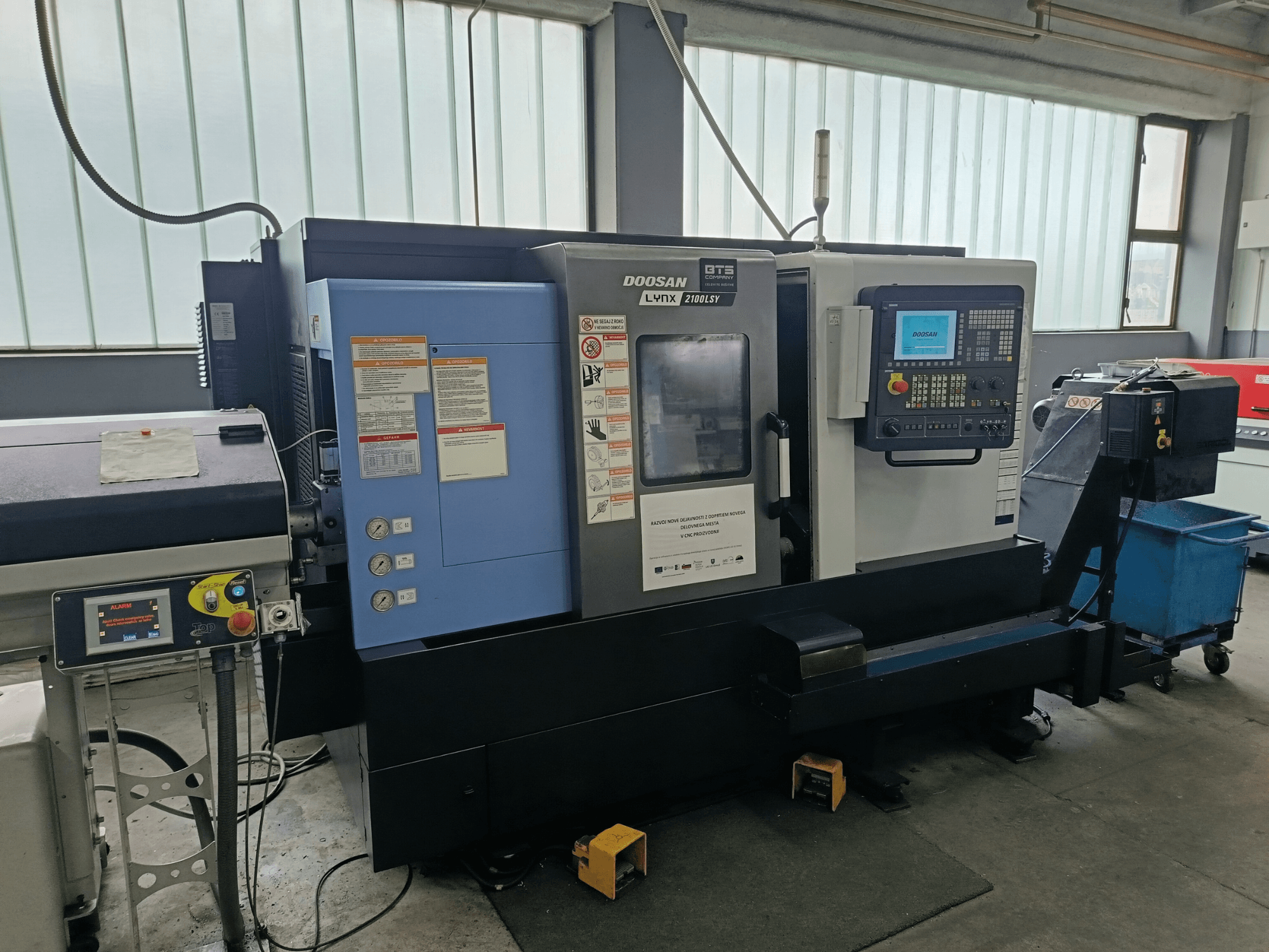 Токарно-фрезерний центр DOOSAN LYNX 2100 LSY, вид збоку з панеллю керування та кнопками керування, з видимими інформаційними наклейками.