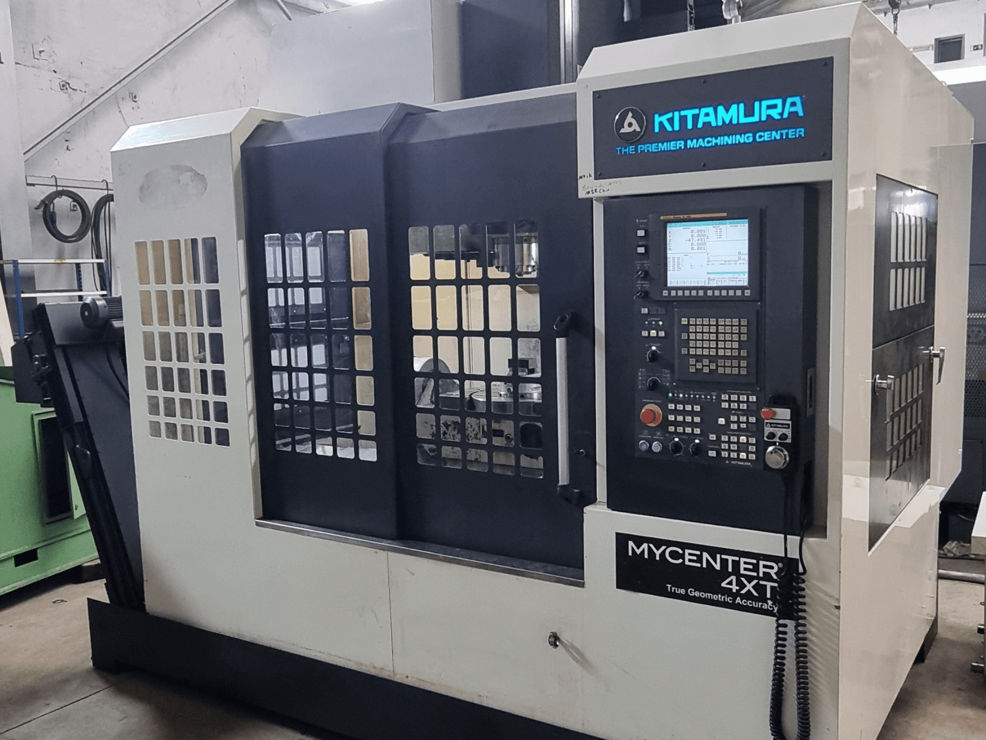 Альтернативний текст: Вертикальний обробний центр Kitamura MYCENTER 4XT, вид спереду, на якому показано панель керування та деталі верстата в умовах цеху.