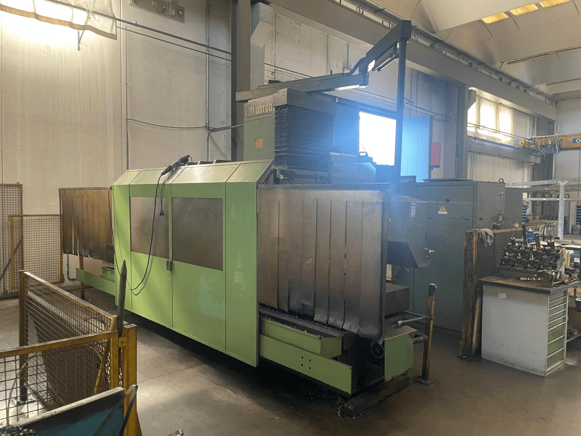 Зелена промислова машина з видимими металевими компонентами, вид спереду; має панель управління, попередження про безпеку та робоче місце поруч.