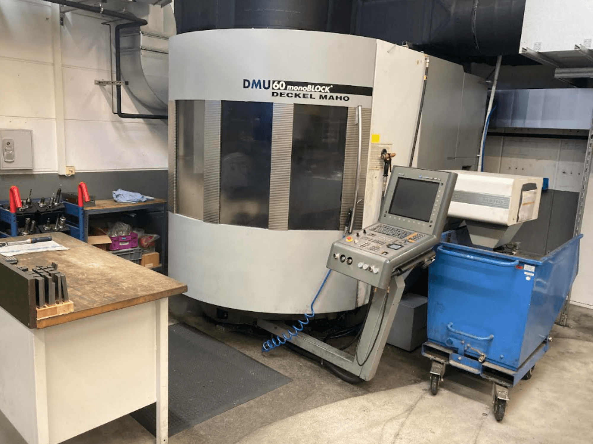 DMG MORI DMU 60 Моноблочний вертикальний обробний центр, вид спереду з панеллю керування, робочою зоною та синім візком для інструментів.