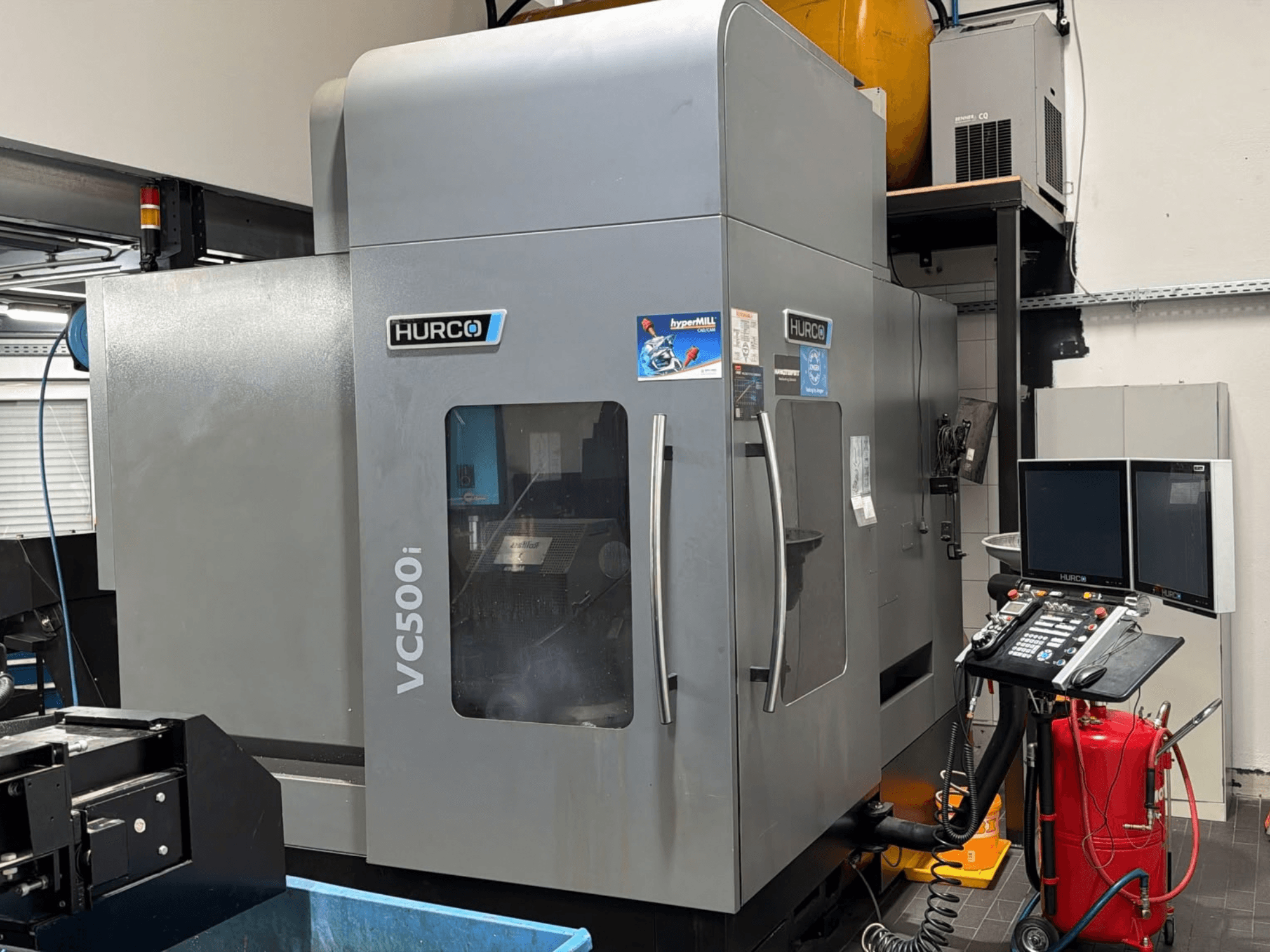 Вертикальний обробний центр Hurco VC500i, вид спереду, на якому видно панель керування та два монітори, у виробничому цеху.