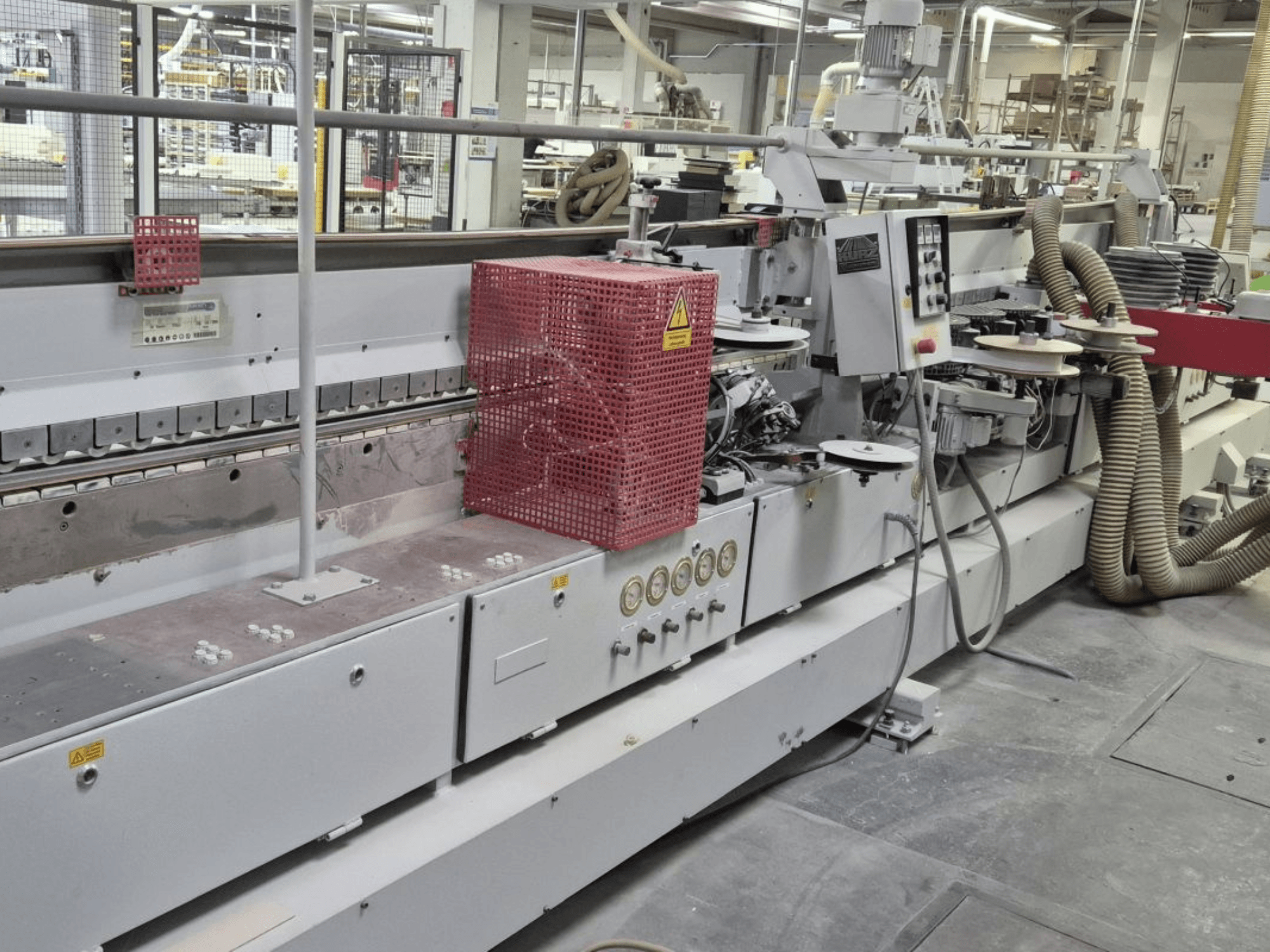 Крайкооблицювальний верстат з панеллю керування, всмоктувальними шлангами та червоною захисною кришкою, вид збоку.