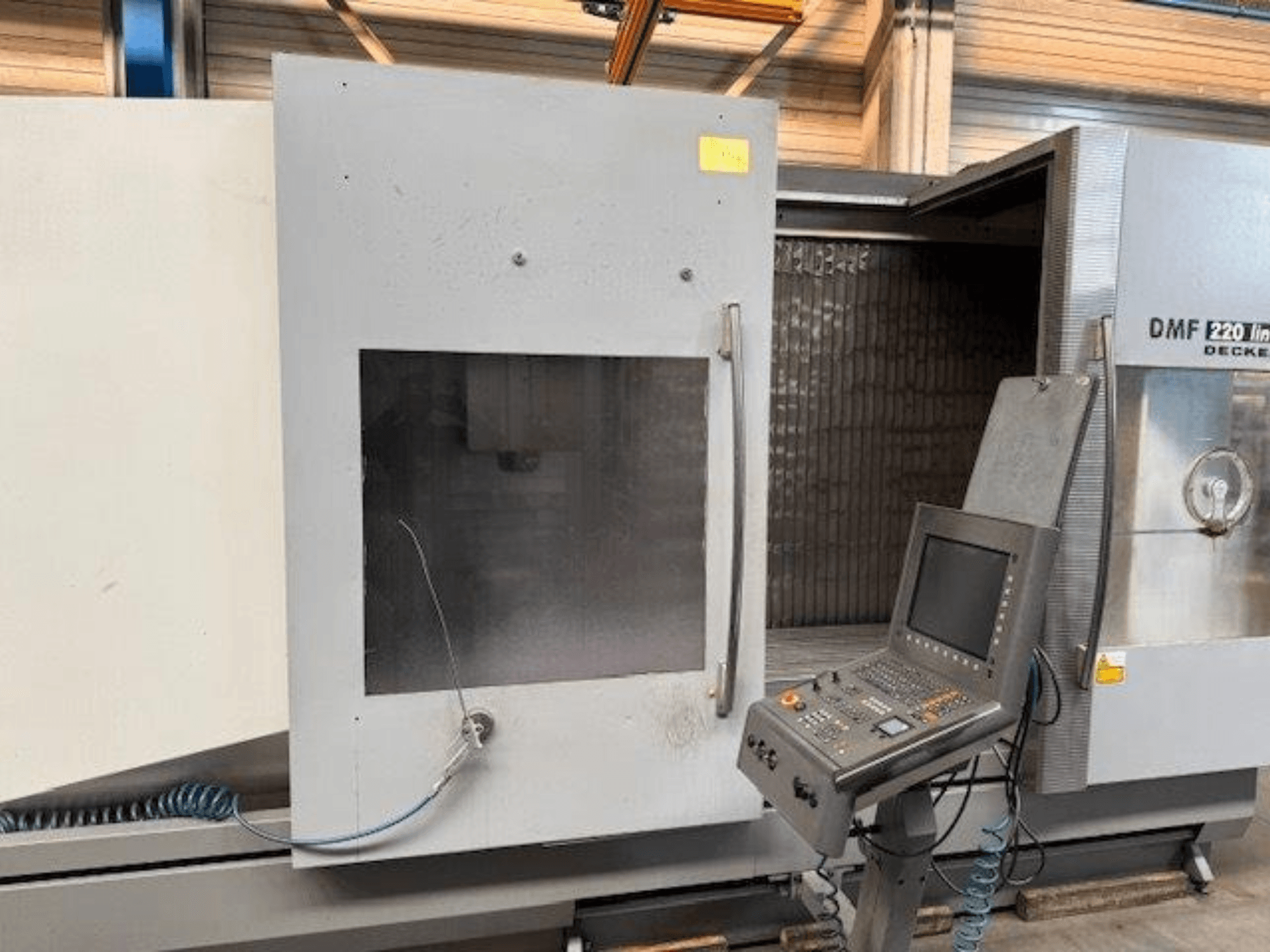 Вид спереду лінійного вертикального обробного центру DECKEL MAHO DMF 220 з панеллю керування та відкритими дверцятами верстата.