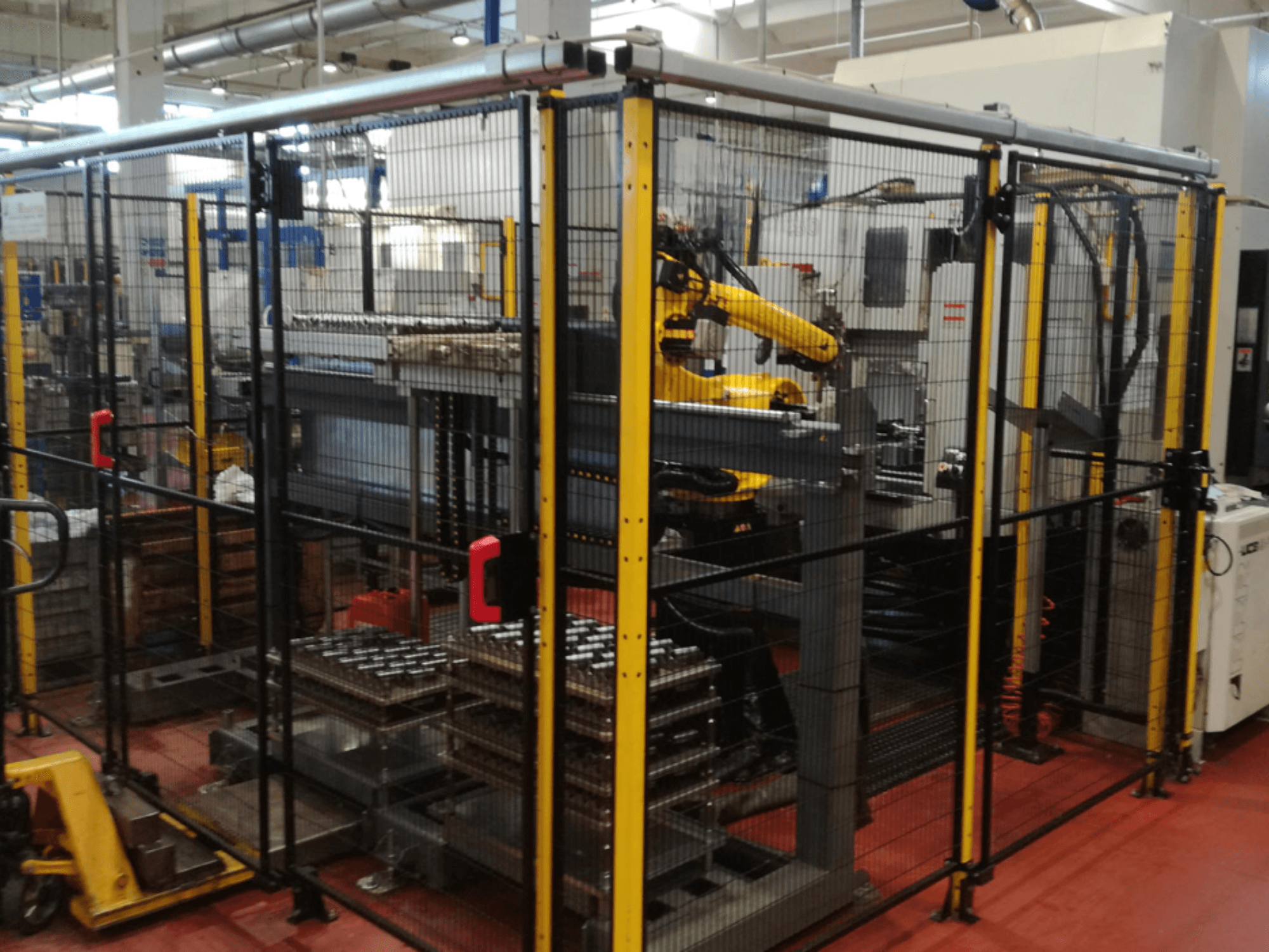 Вертикальний обробний центр Enshu EV450 в огородженому робочому просторі, з роботизованими маніпуляторами і декількома штабелями заготовок. Вид спереду.