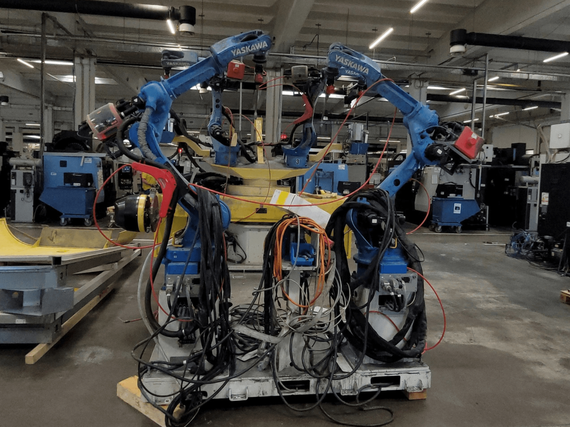 Роботизована зварювальна лінія Yaskawa RWC L1_OS 15330, вид спереду, з двома синіми роботами, оснащеними довгими кабелями та зварювальним інструментом.