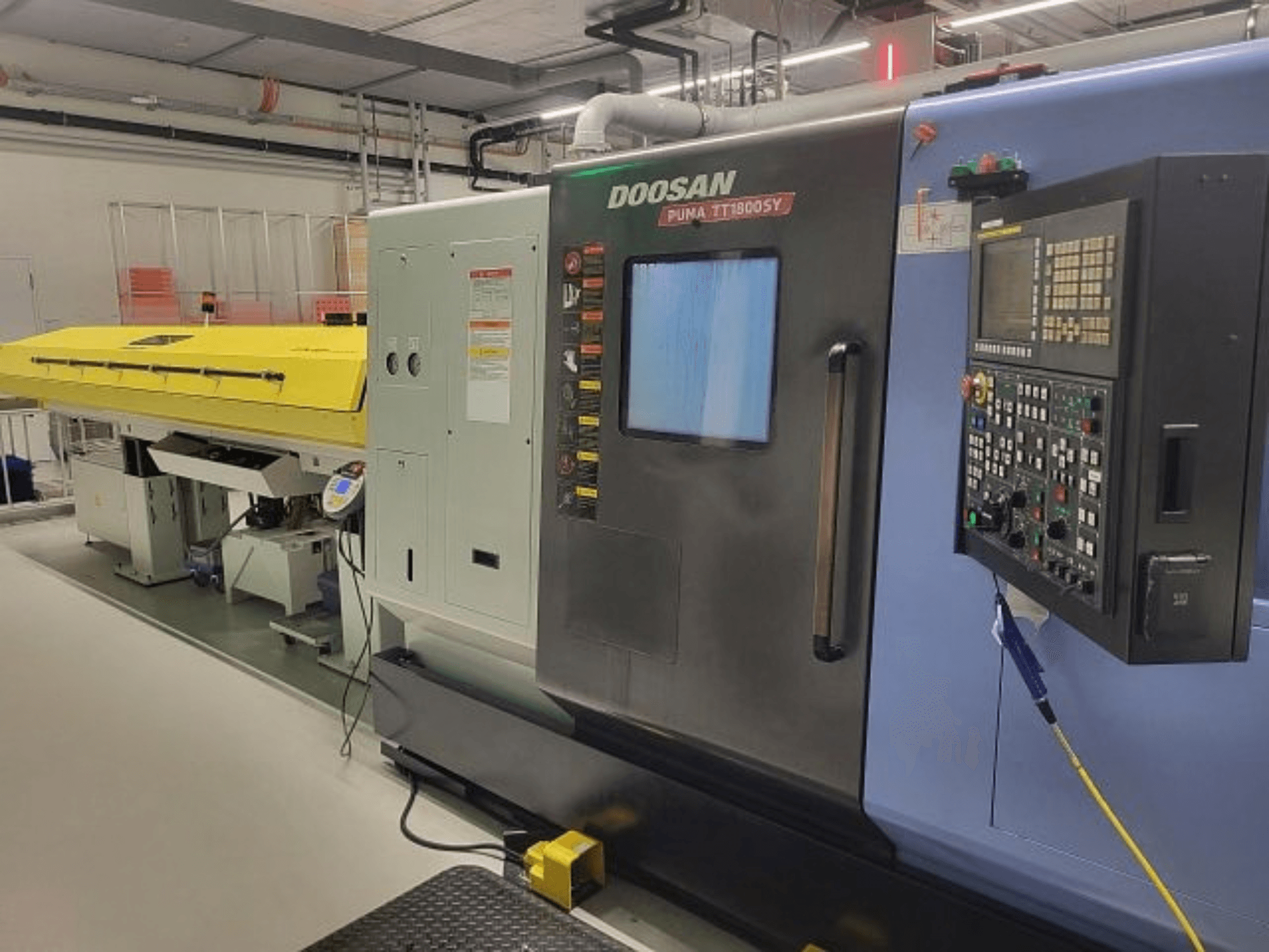 Токарно-фрезерний центр DOOSAN PUMA TT 1800 SY, вид спереду з панеллю керування та жовтою кришкою, промислове середовище.