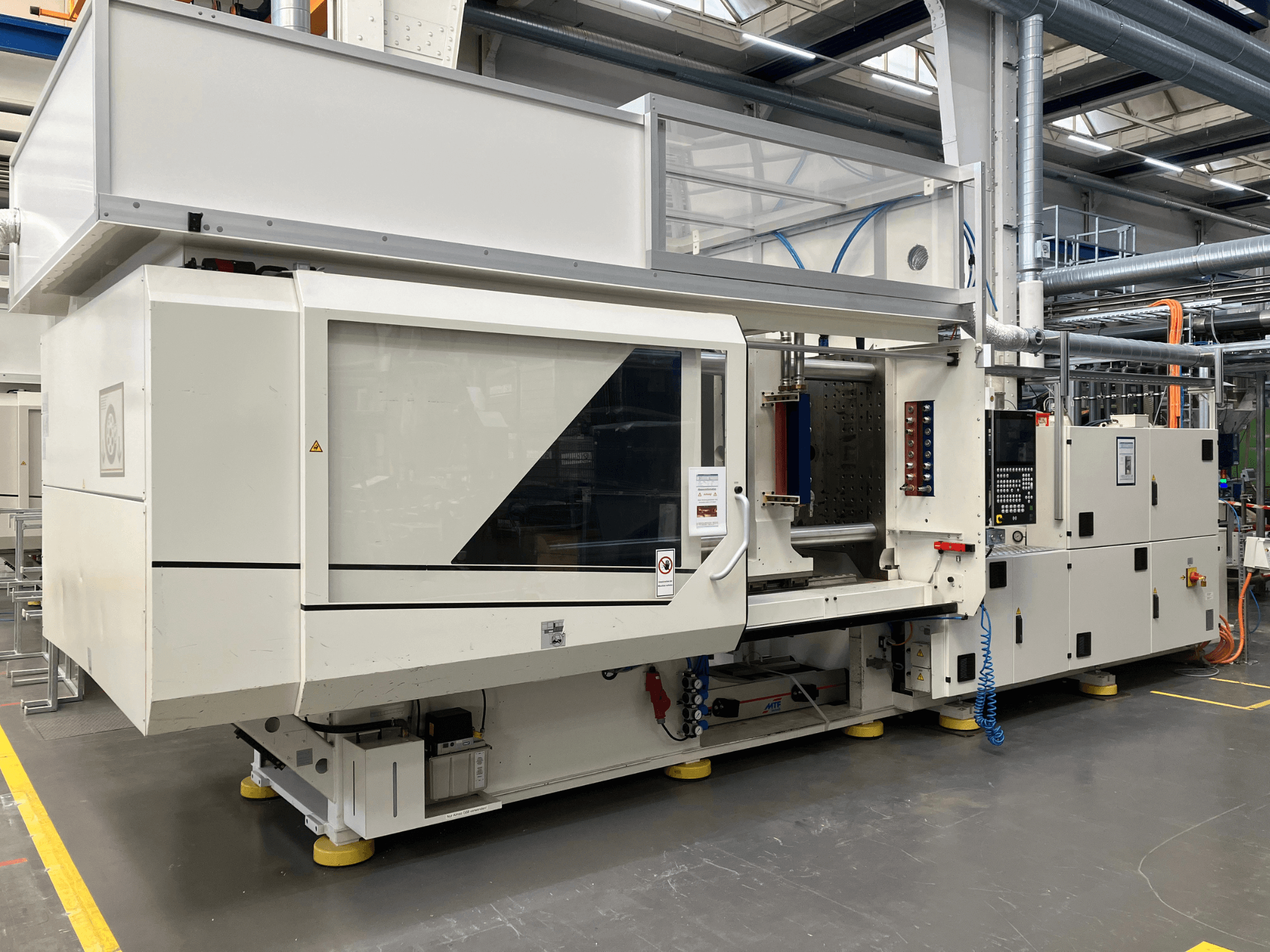 Вид збоку на термопластавтомат моделі AET з панеллю керування та прозорими кришками в промислових умовах.