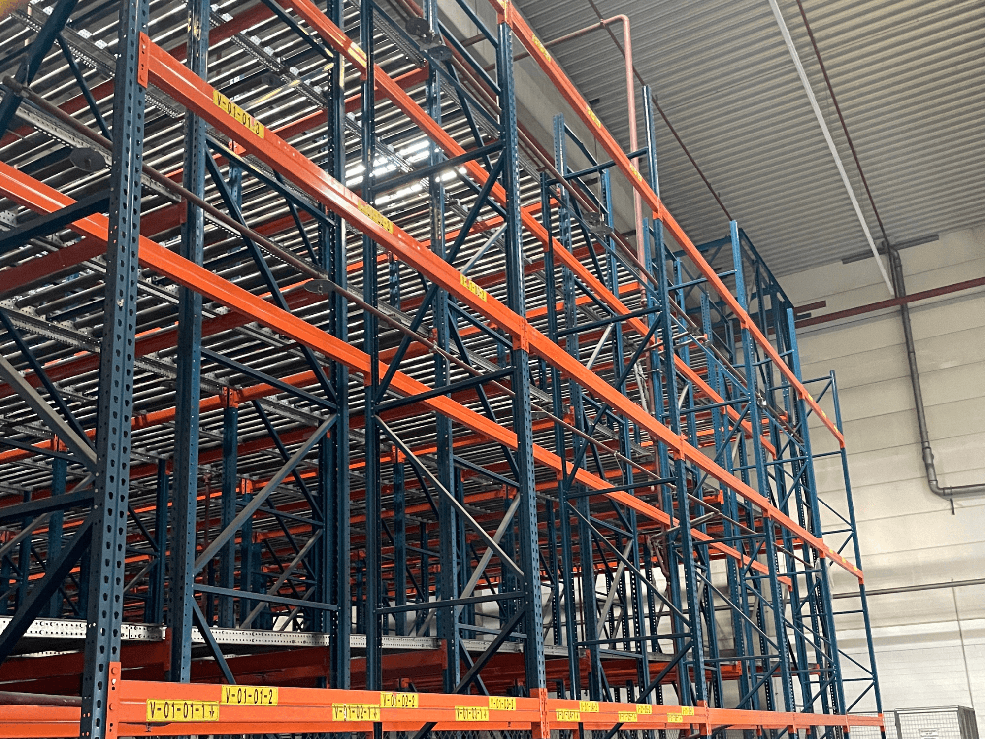 FL SYSTEME F05.10 Система обробки палет FLG на складі, показана збоку, з надміцними оранжево-синіми стелажами.