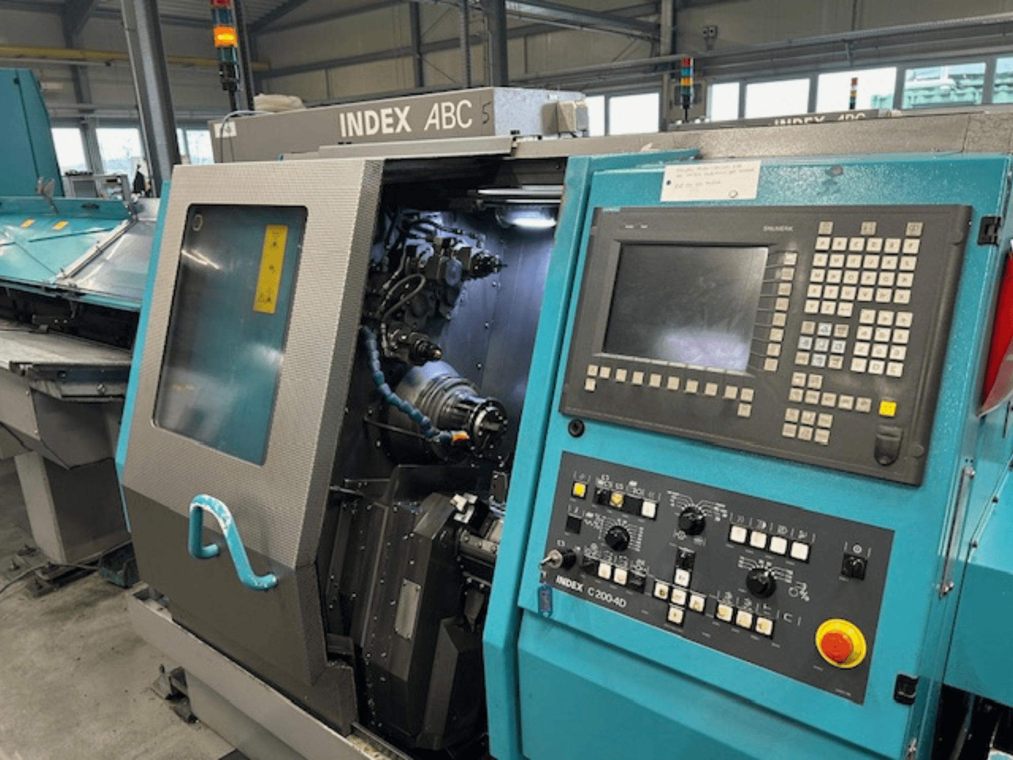 Вид спереду токарного верстата з ЧПК INDEX C200-AD з панеллю керування, видимими внутрішніми компонентами та елементами безпеки.