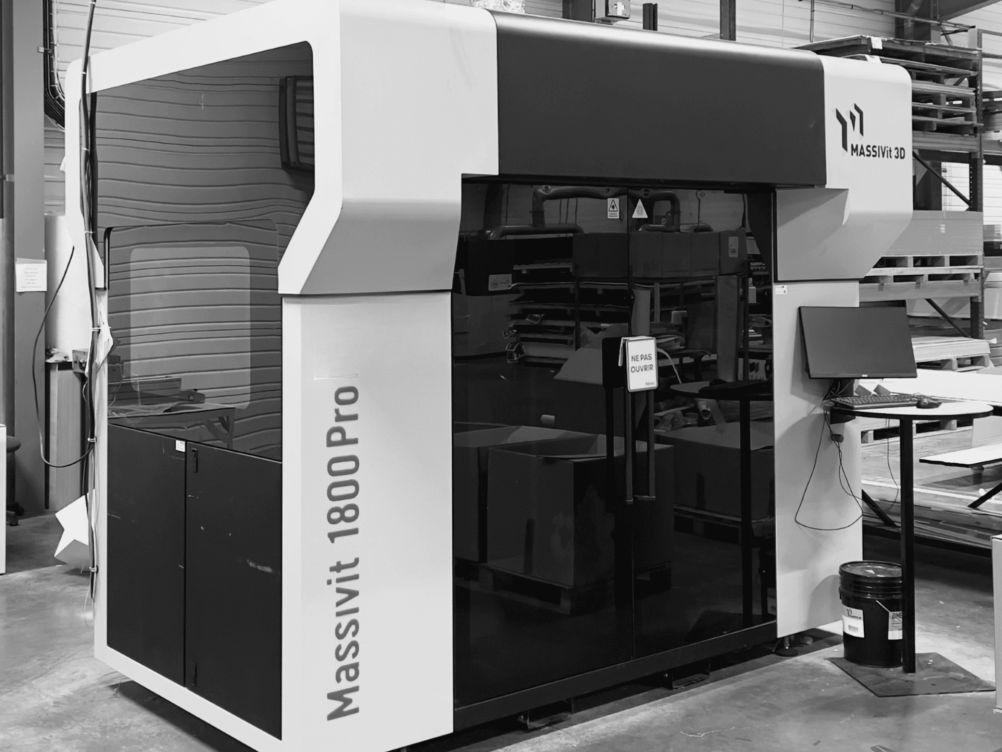 Пластиковий 3D-принтер MASSIVIT 1800 PRO у майстерні, вид спереду, на якому видно комп’ютерну робочу станцію та панель керування.