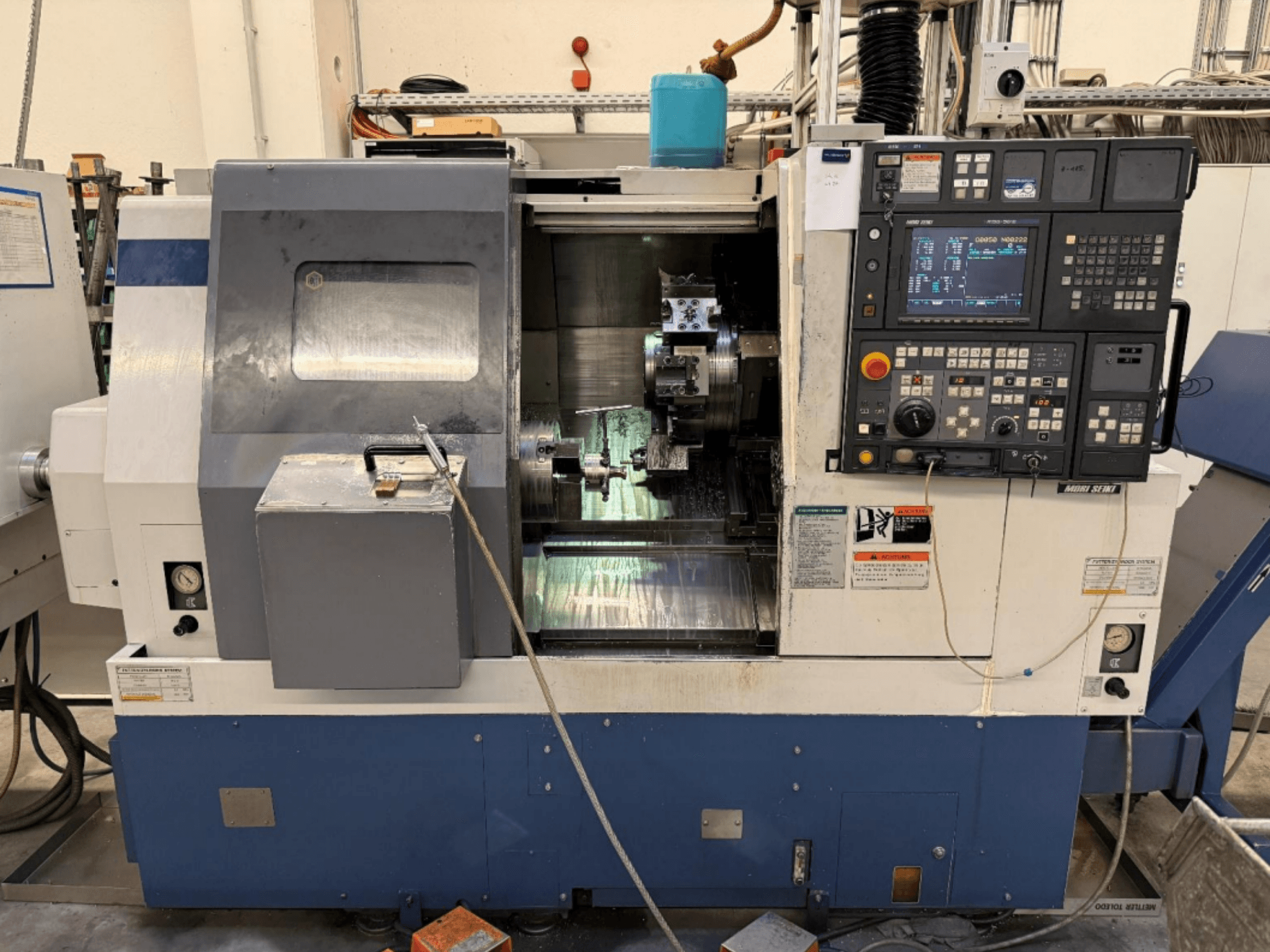 Токарно-фрезерний центр MORI SEIKI SL-250ASMC, вид спереду, на якому видно панель управління та патрон для затискання заготовки в процесі роботи.