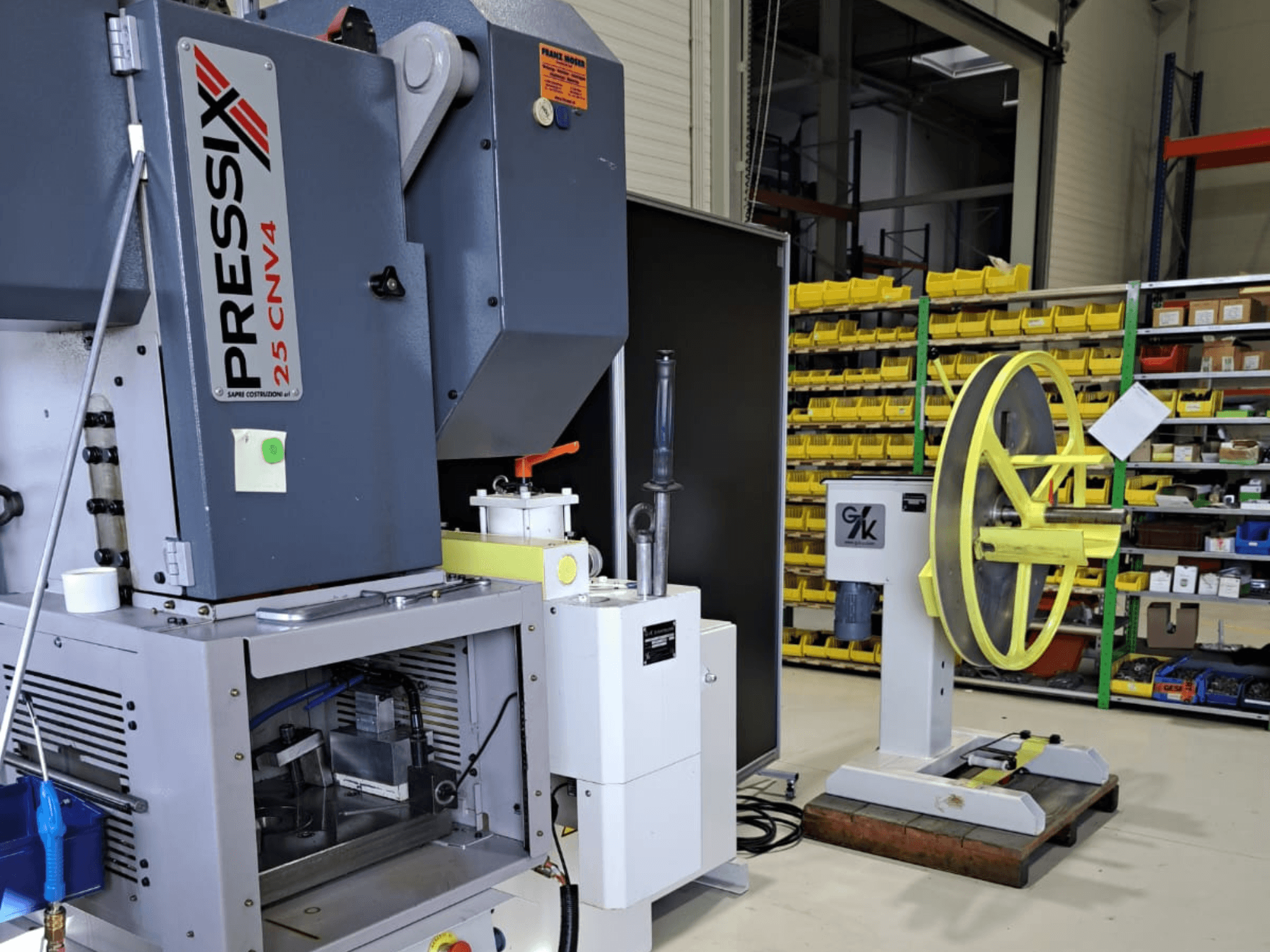 Промисловий верстат з PRESSIX 25 CNV4 ліворуч і жовтим колесом, встановленим на сірій основі праворуч, вид спереду.