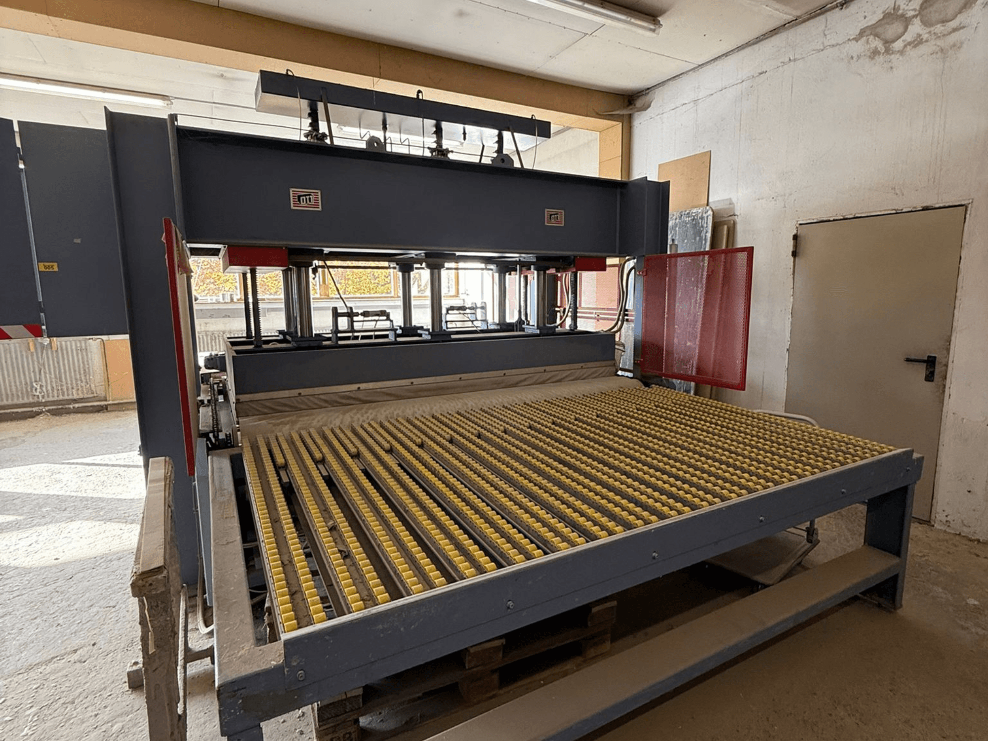 Промислова машина з жовтими роликами, вид спереду, видно логотип бренду, використовується для обробки матеріалів в умовах майстерні.