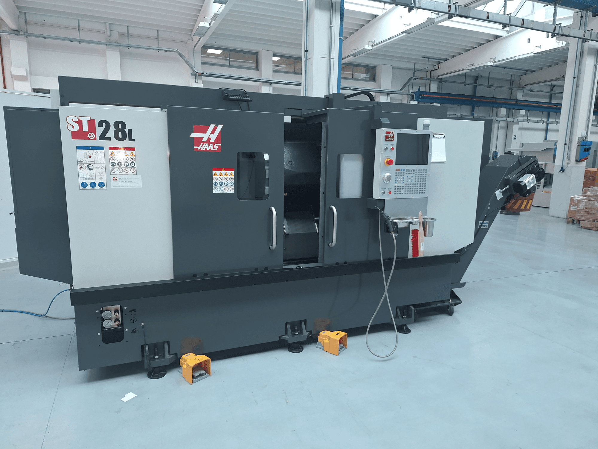 Бічний вигляд горизонтального токарного верстата Haas ST-28L із панеллю керування, робочими кнопками та попереджувальними наклейками.