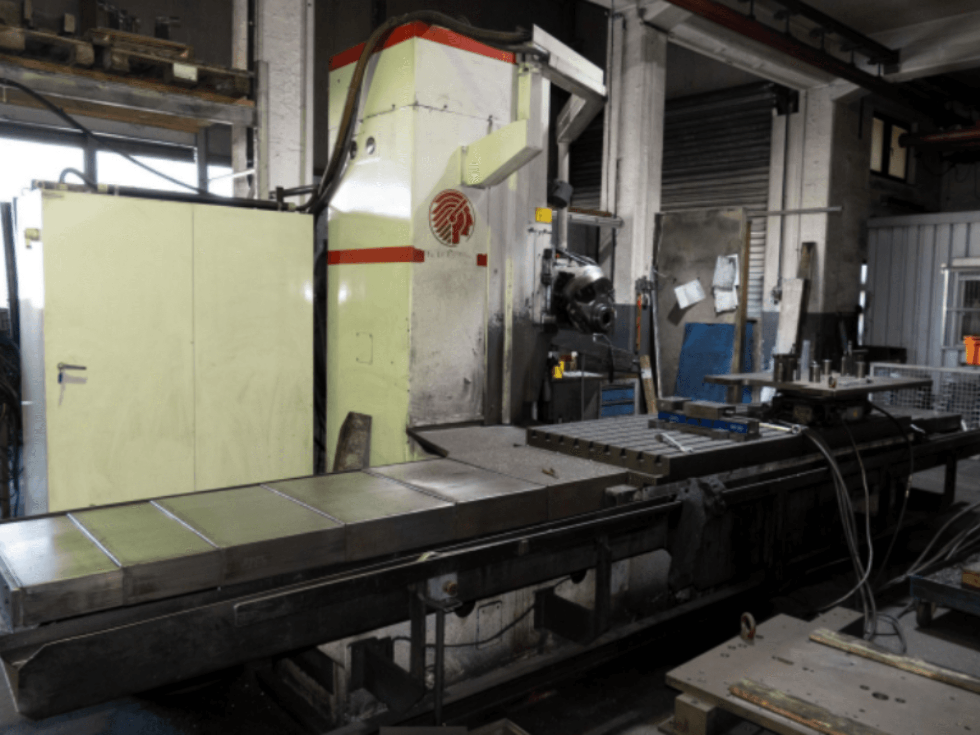 Промисловий фрезерний верстат з великим столом, вид збоку, що демонструє елементи керування та навісне обладнання в умовах майстерні.