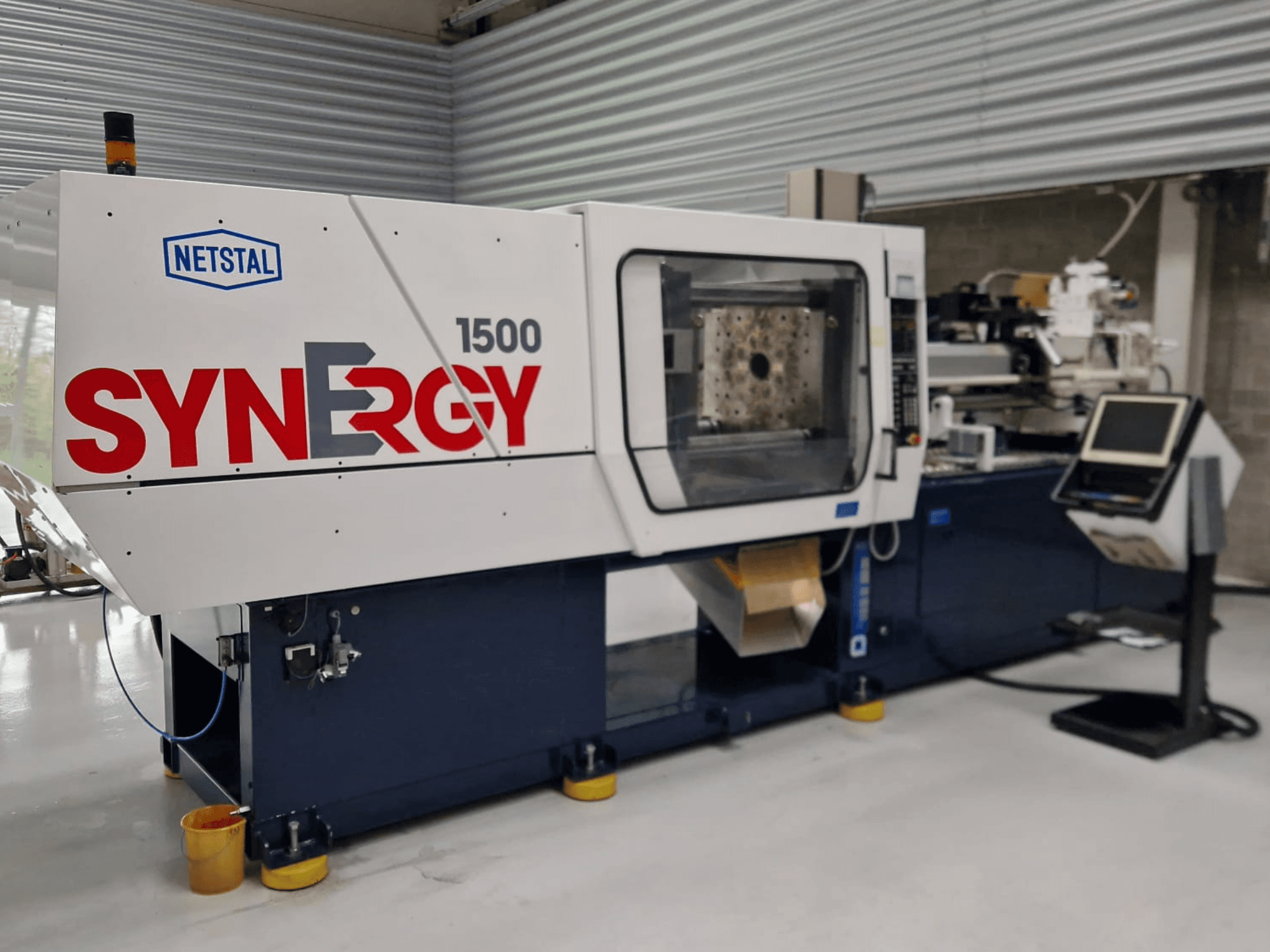 Гідравлічний термопластавтомат Netstal Synergy 1500-460, вигляд спереду, демонстрація панелі керування та відкритої зони впорскування.